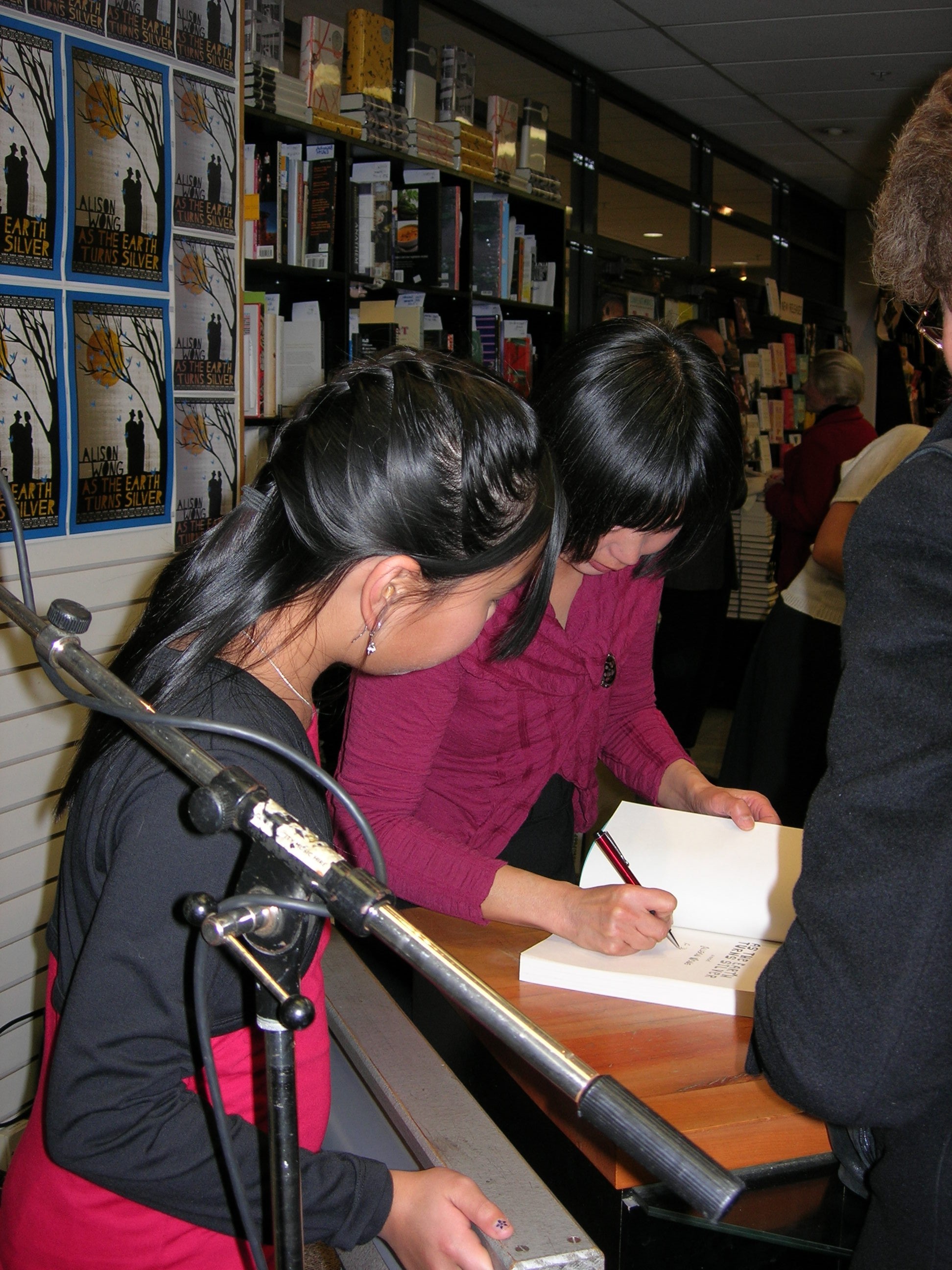 A woman wearing a burgundy knit signing books at a wooden table