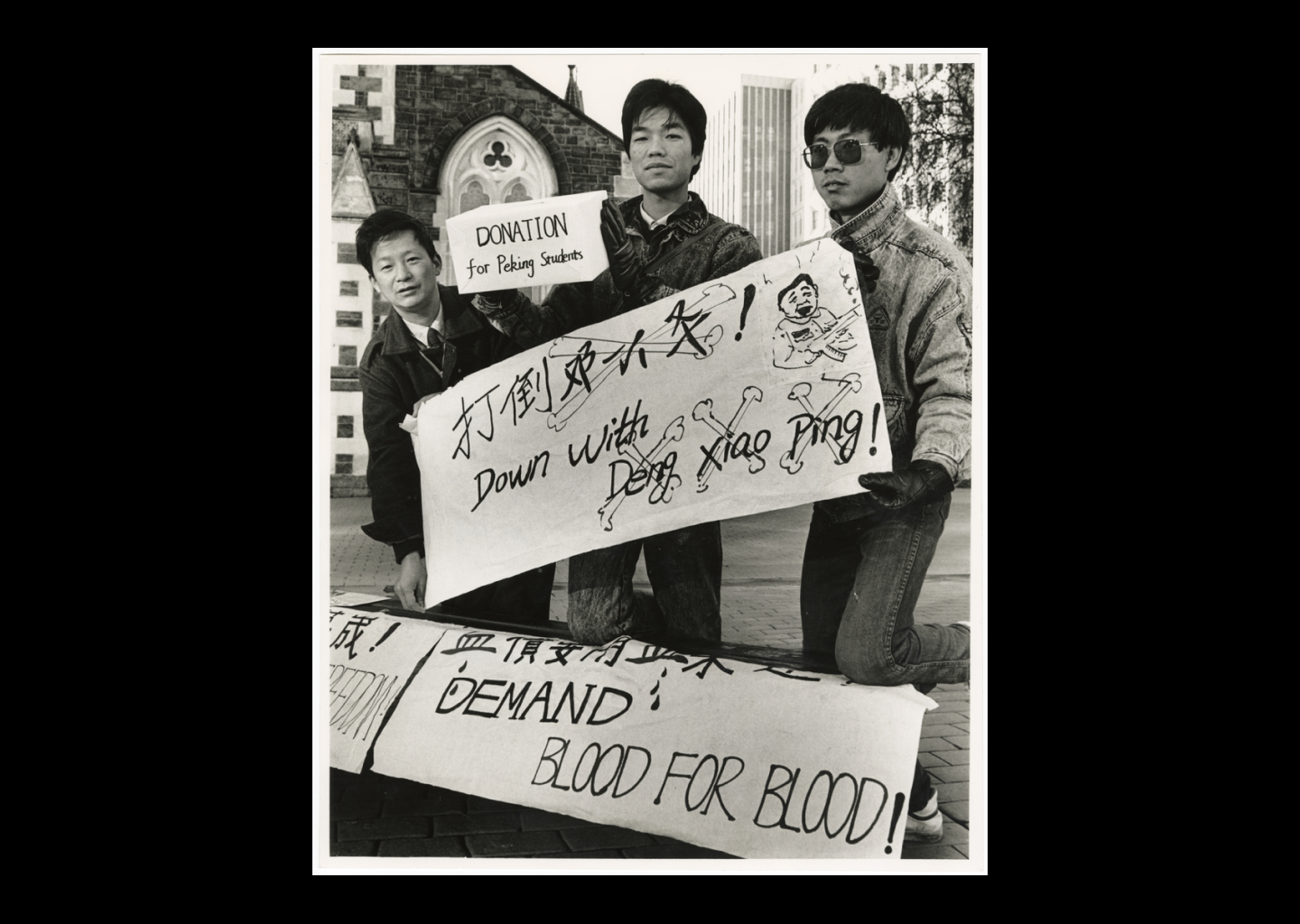 Three Chinese students hold protest signs in front of a gothic church.