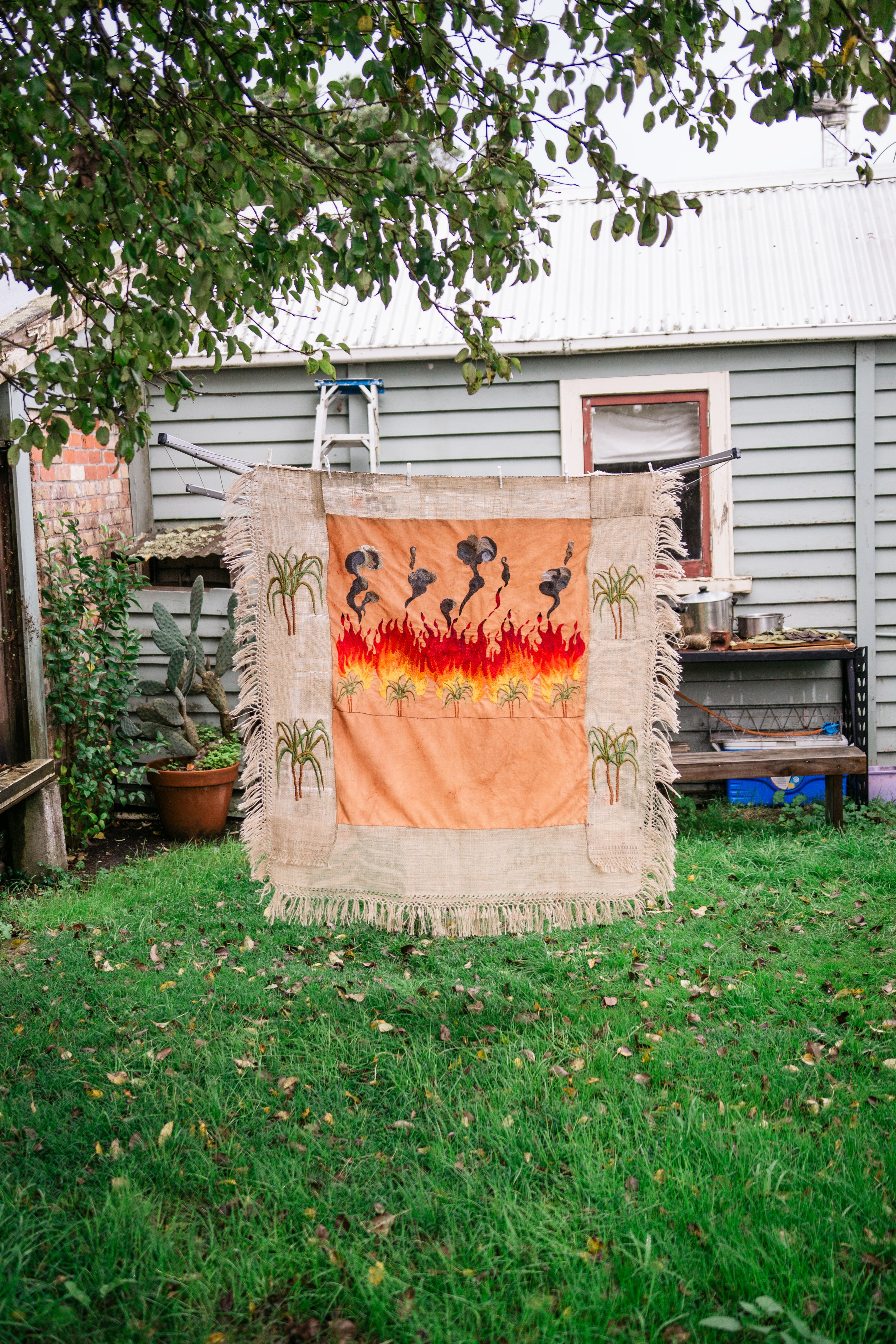Fabric work hanging on a line featuring sugarcane trees burning