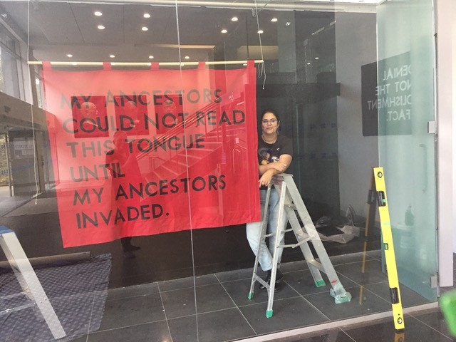 A red banner hanging in a space behind glass next to a person on a ladder