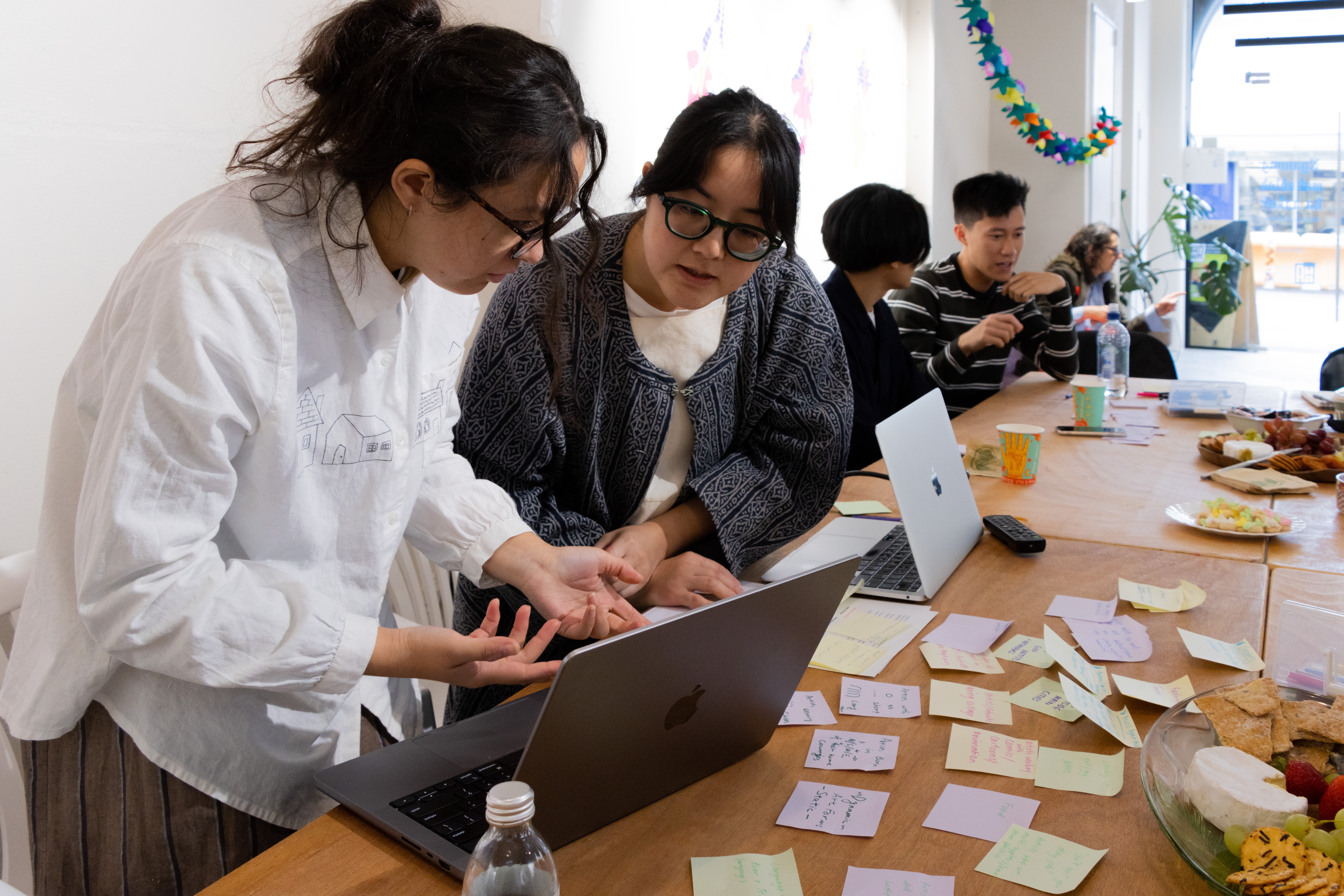 Two people wearing glasses stand in front of a table with laptops surrounded by post-it notes