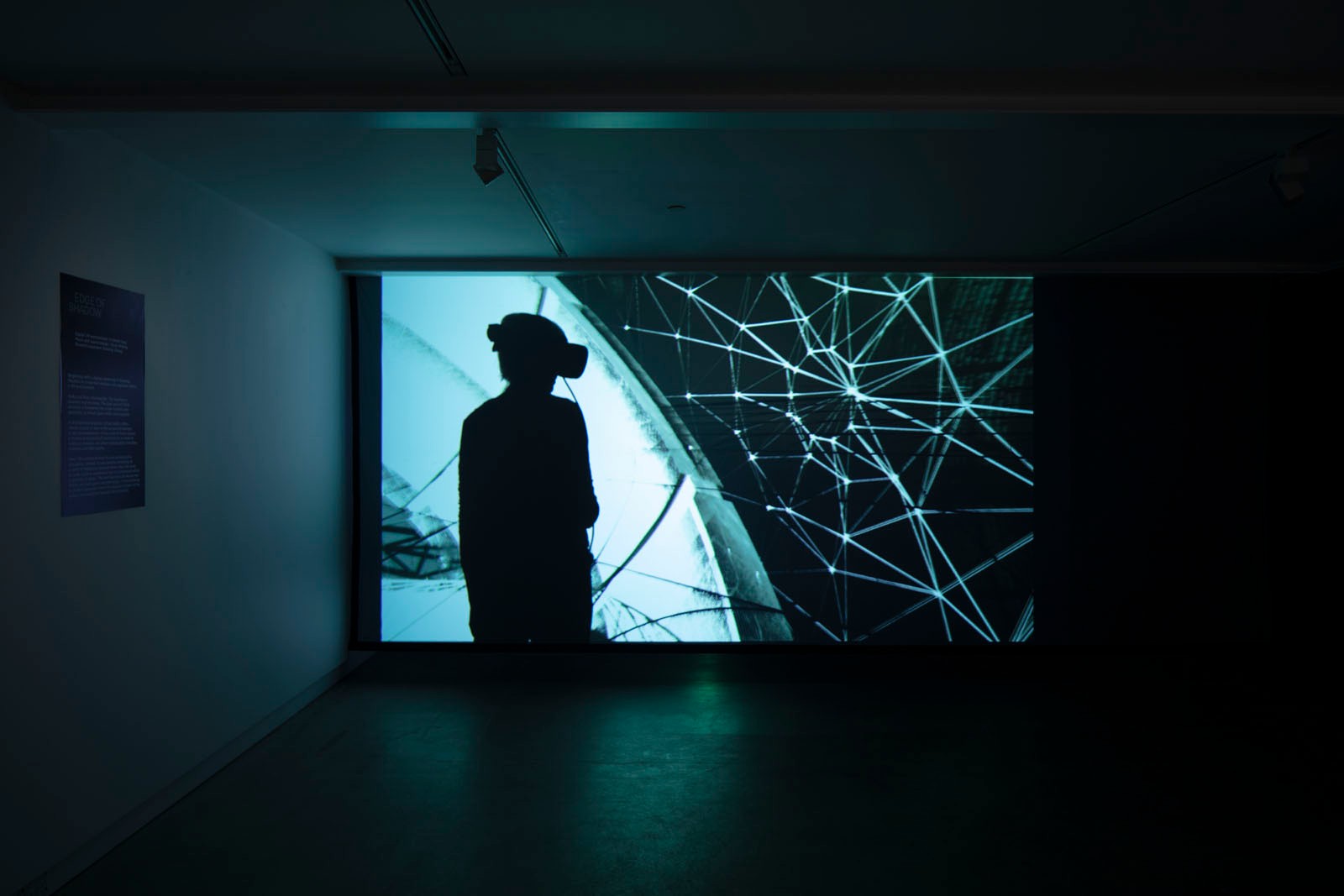 A person stands in a darkened room looking at a video projection.