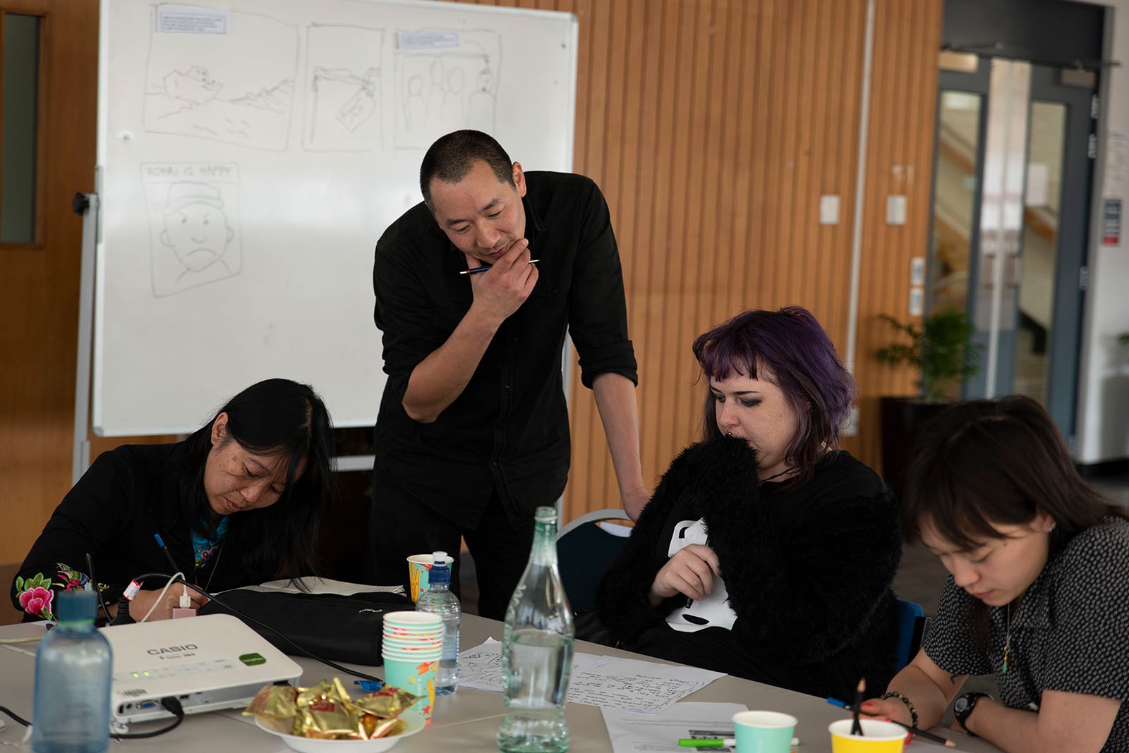 Ant Sang looks at a student's drawing while other students work around them.