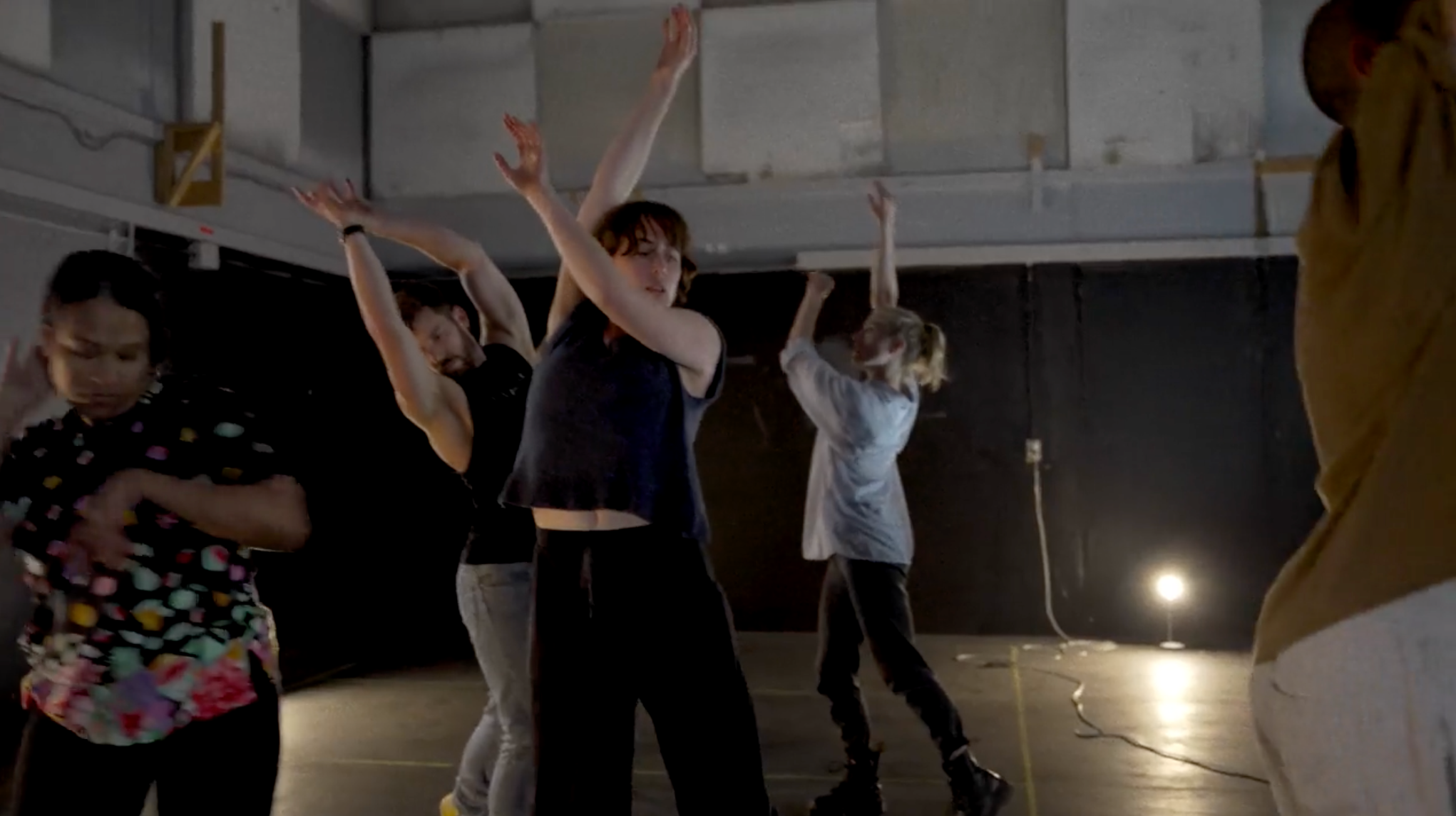 A group of people in a rehearsal space with arms raised in the air, mid-movement