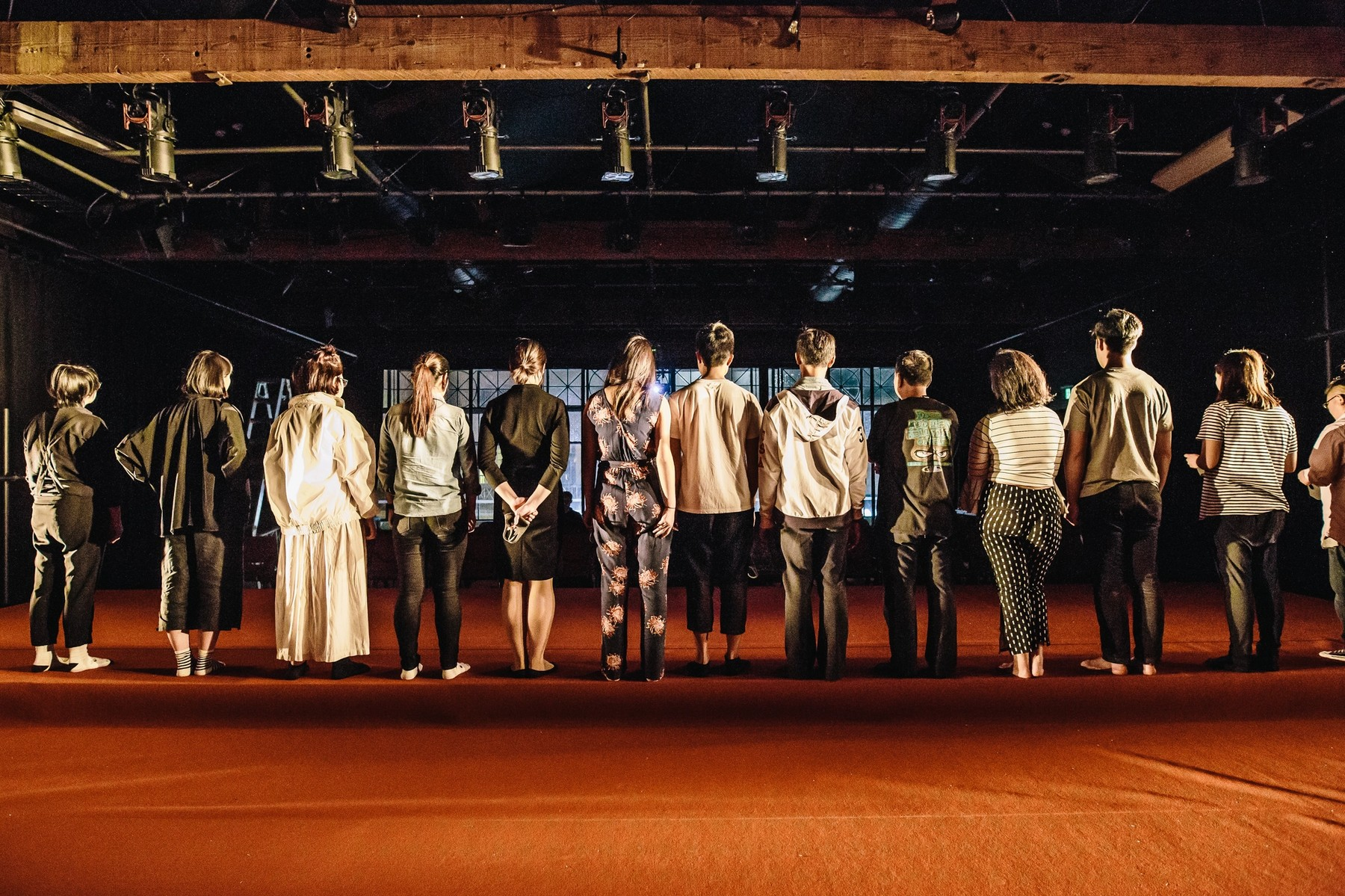 A line of performers on a stage with their backs to us.