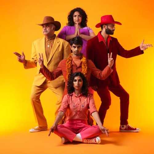Five South Asian actors in warm-toned Desi Cowboy outfits pose direct to camera, throwing peace signs, prayer signs and finger guns against a bright orange background.