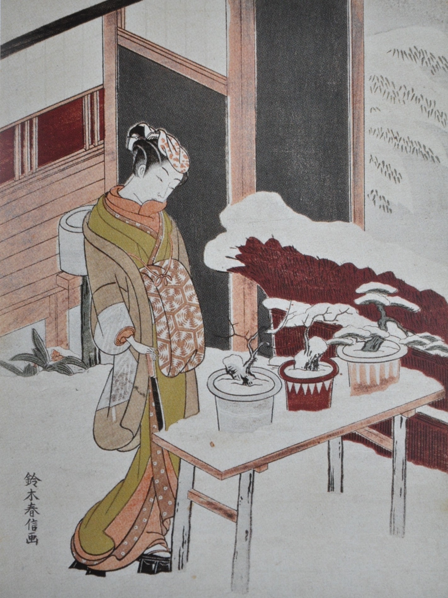 A Japanese woman standing in the snow looking at three bonsai trees.