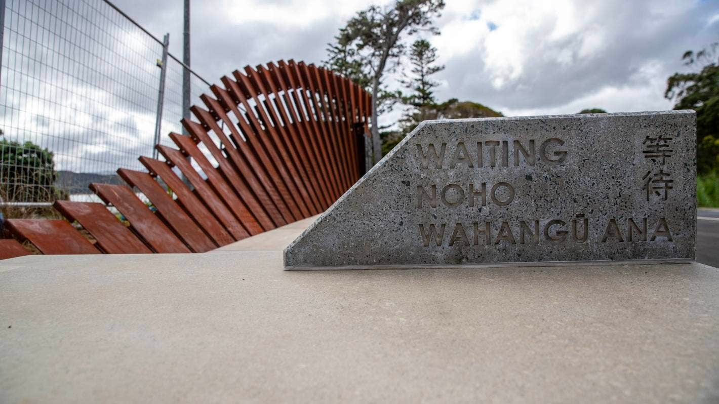 A concrete plaque that says 'Waiting Noho Wahangū Ana' with a curved series of narrow steel panels behind