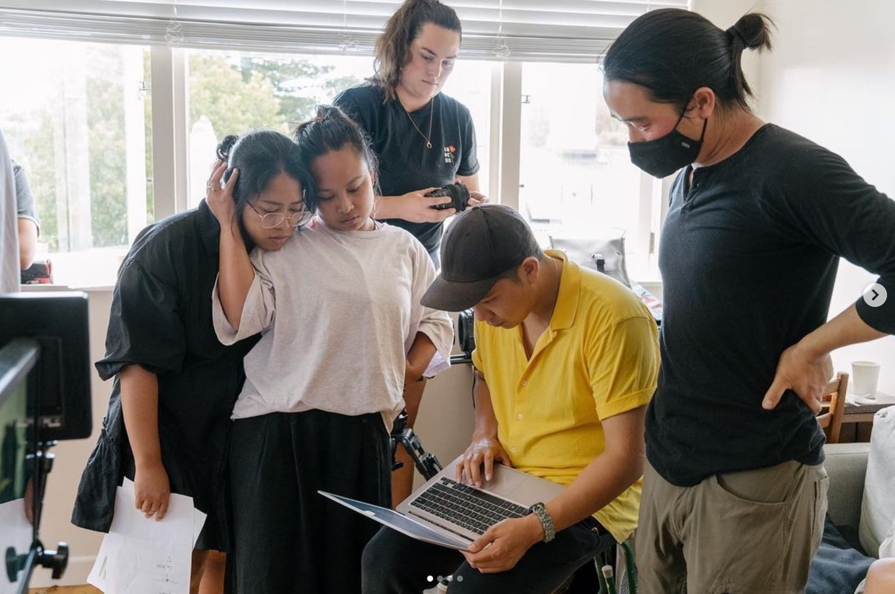 Five people inside a living room looking at an open laptop