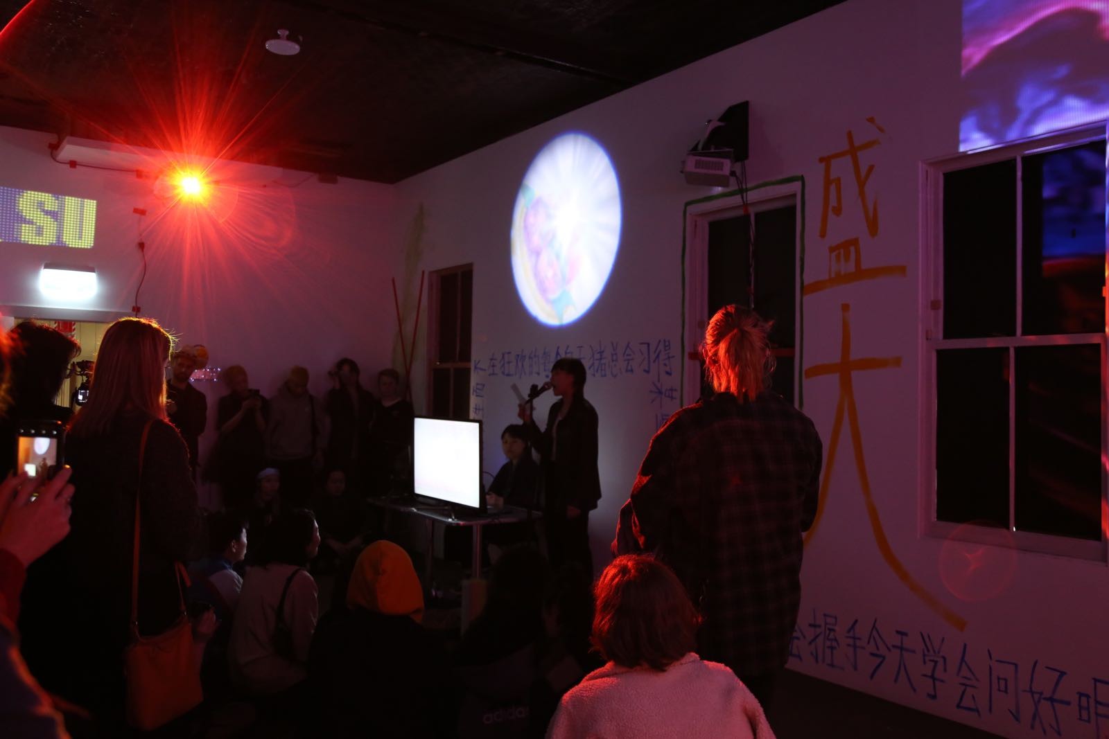 Two artists in a crowded room that is darkly lit with projections and coloured lighting.