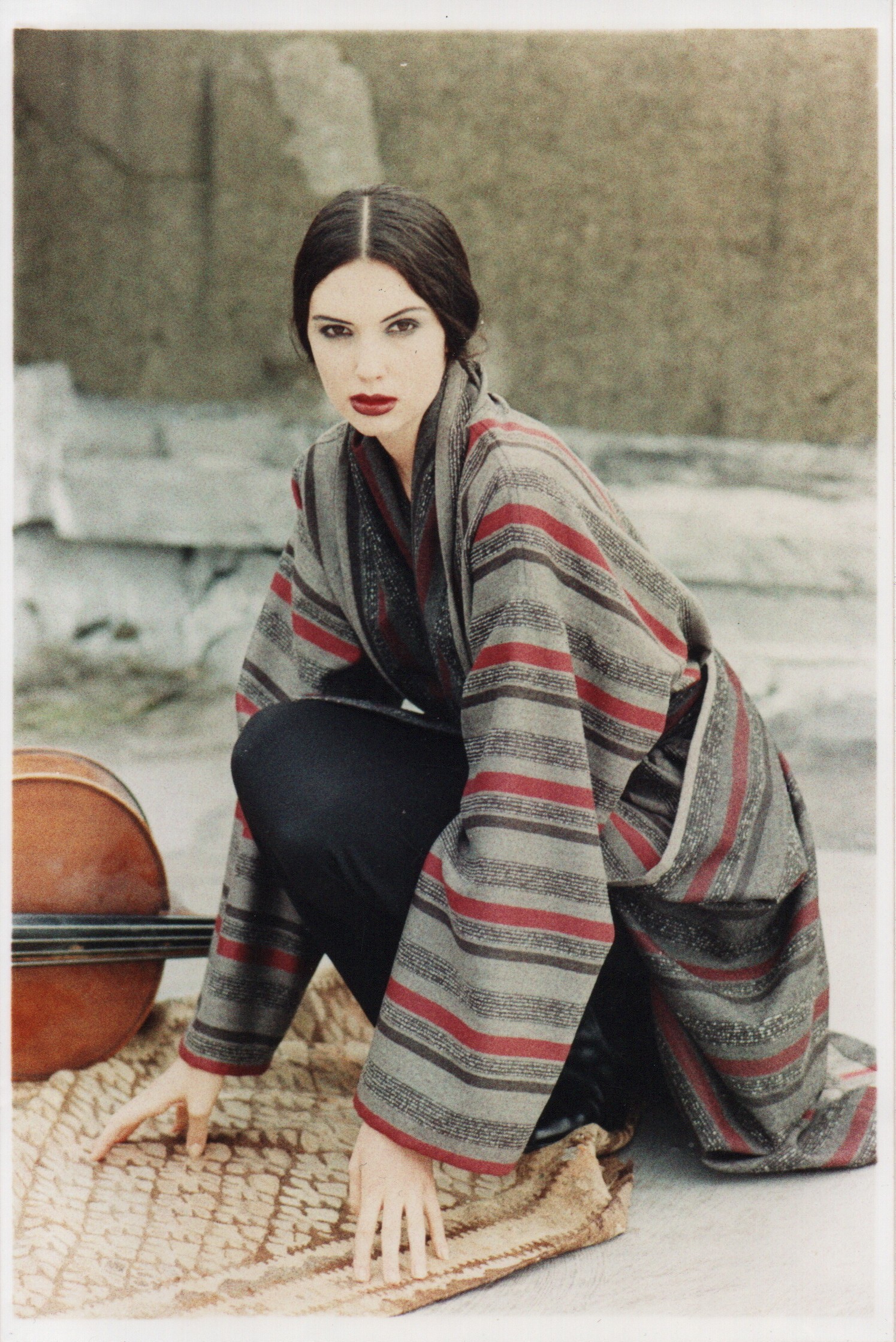 A photo of a woman with a wide striped woolen fabric in greys and red detail crouched to the ground