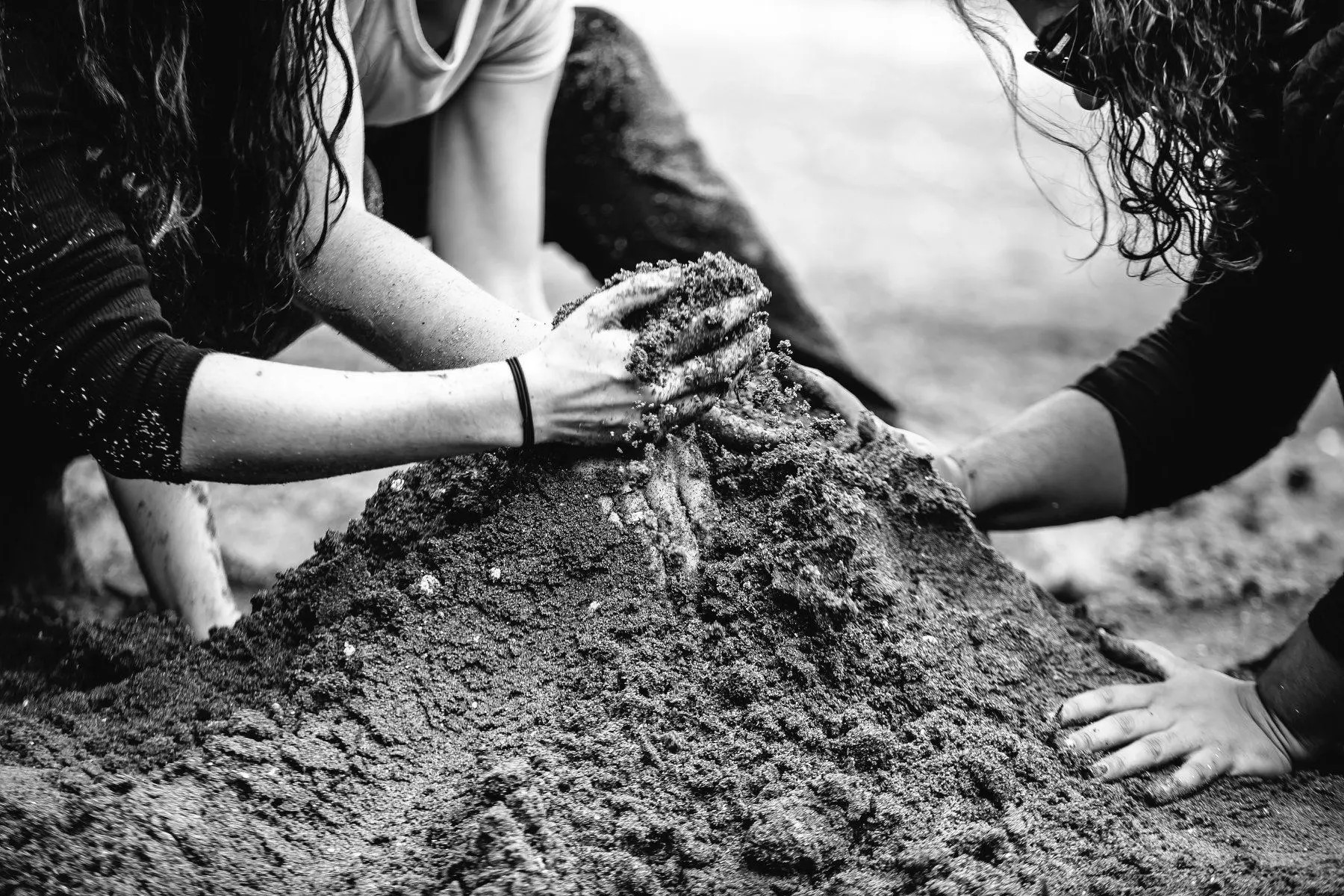 A close-up of a single pile of sand with three hands