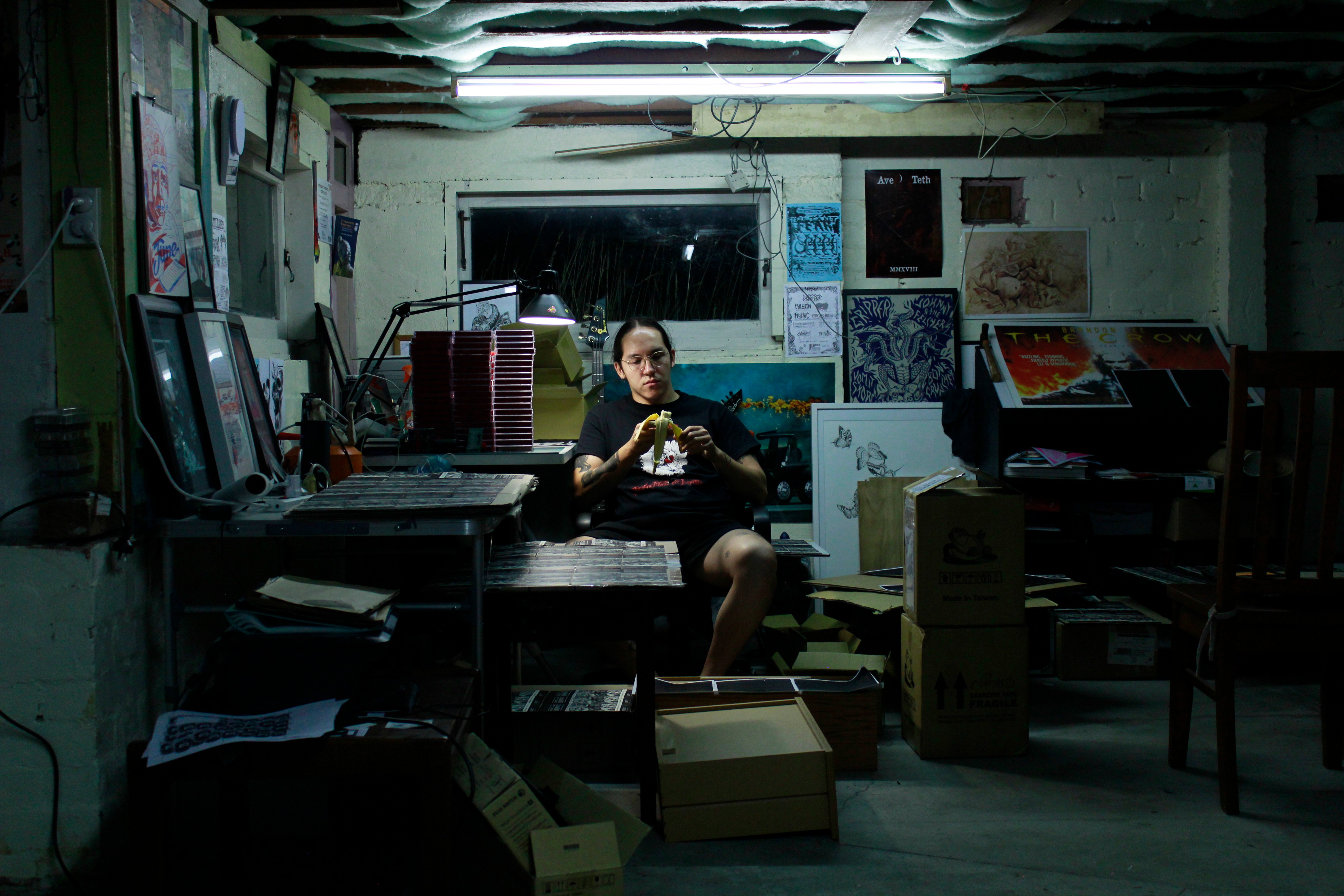 A person in a dimly lit artist studio creating work. Various pieces of art and posters are on the walls.