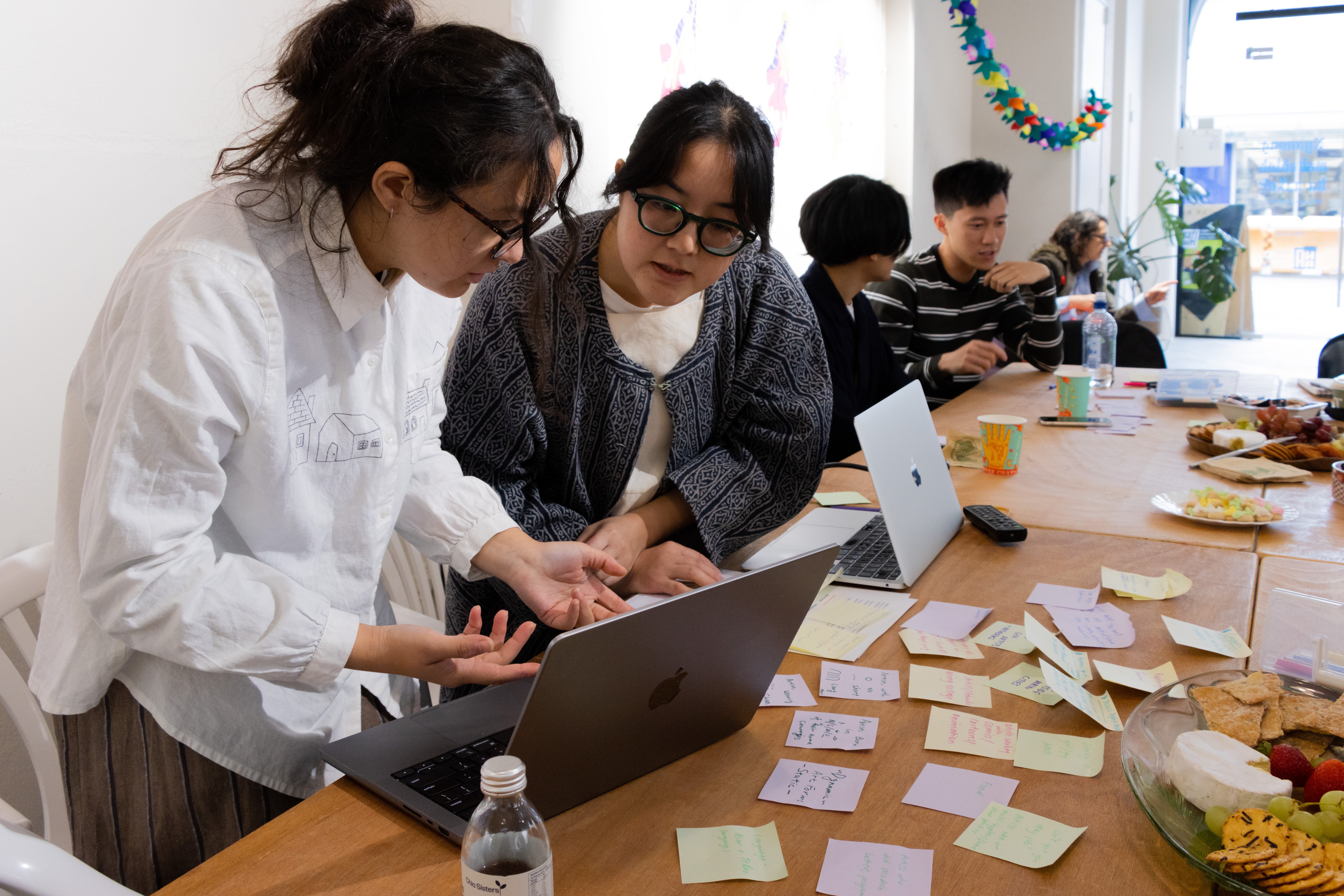 Jenn Cheuk and Emma Ng look at a laptop at a busy table covered in post-it notes.