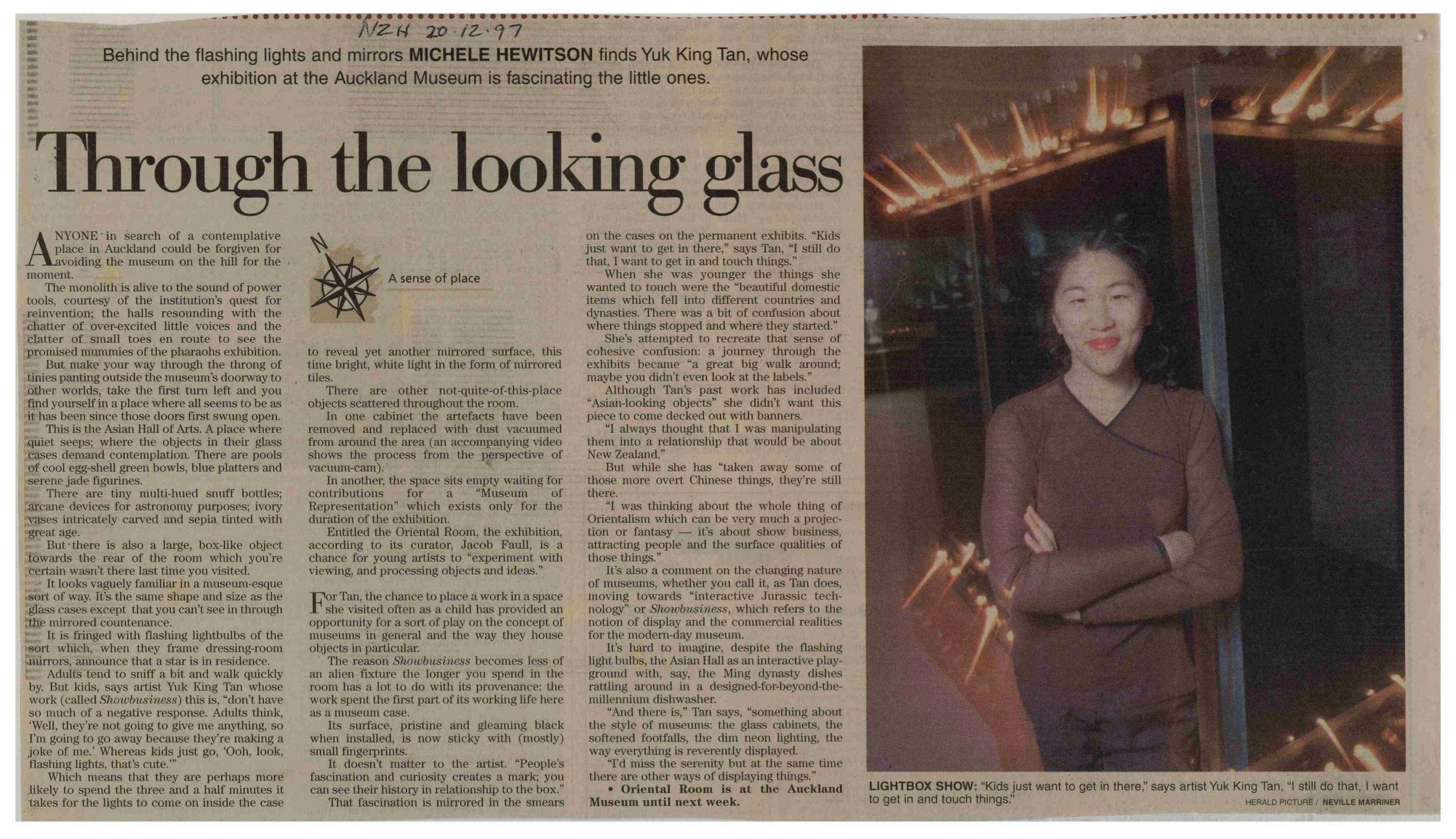 Newspaper clipping with photo of Yuk King Tan with arms crossed in front of a lit-up artwork in the museum.