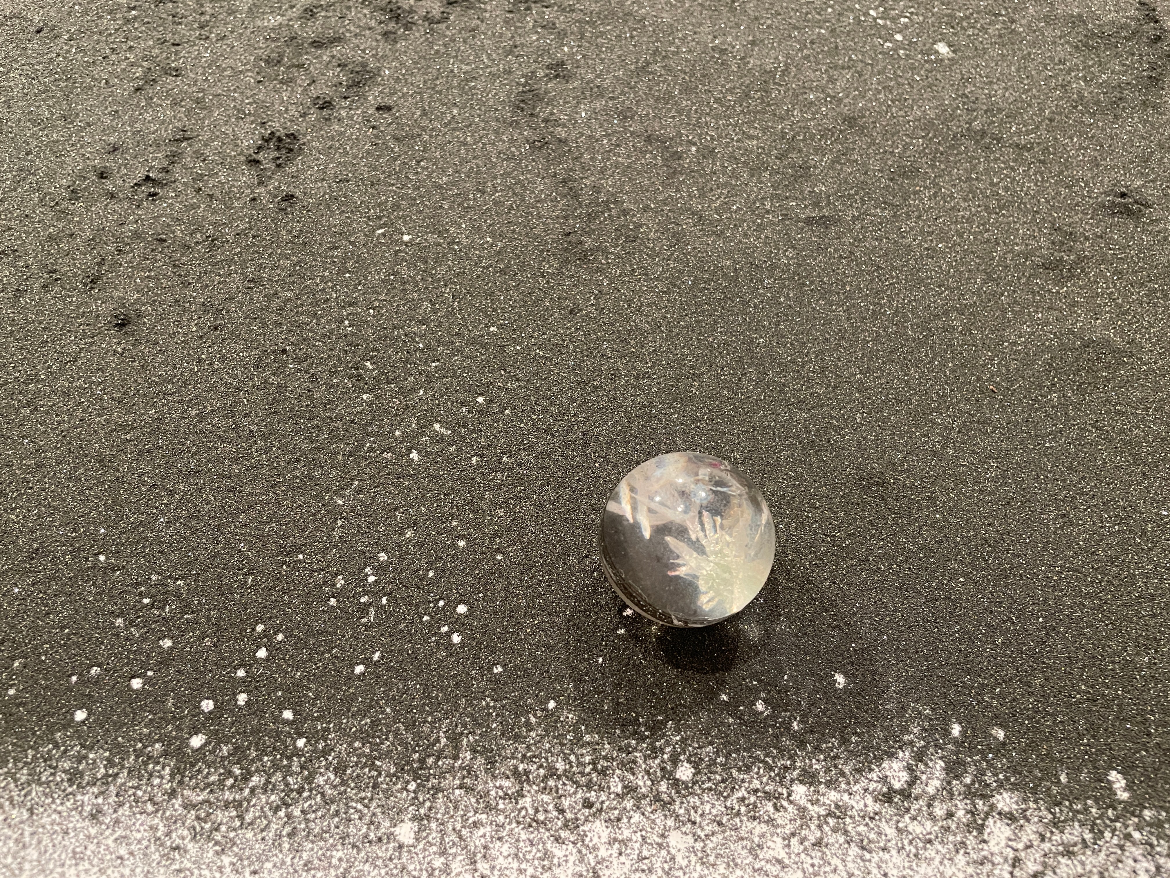 A clear sphere on top of black sand with a white ground visible