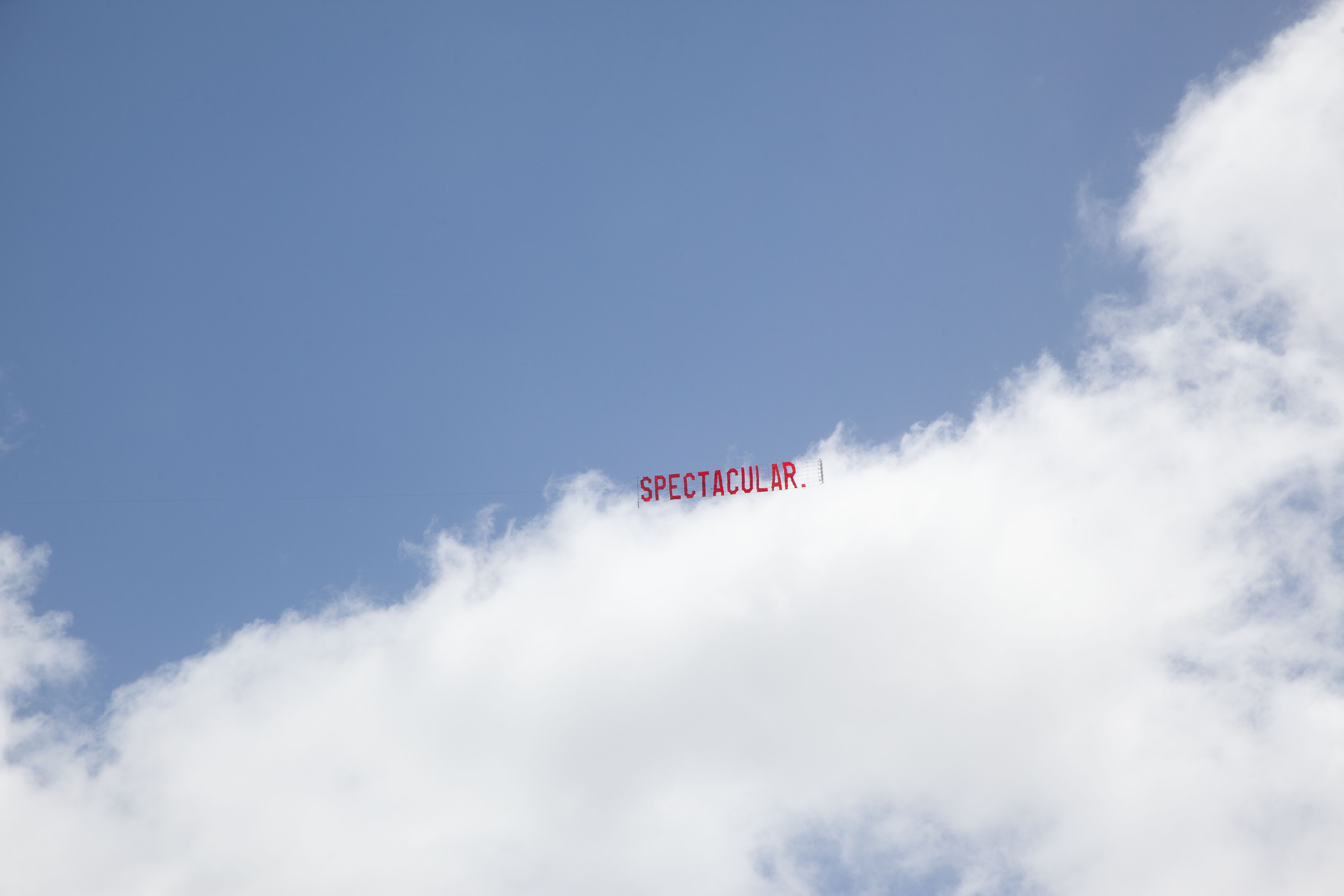 A sign being flown by a plane in red capital letters, 'SPECTACULAR'