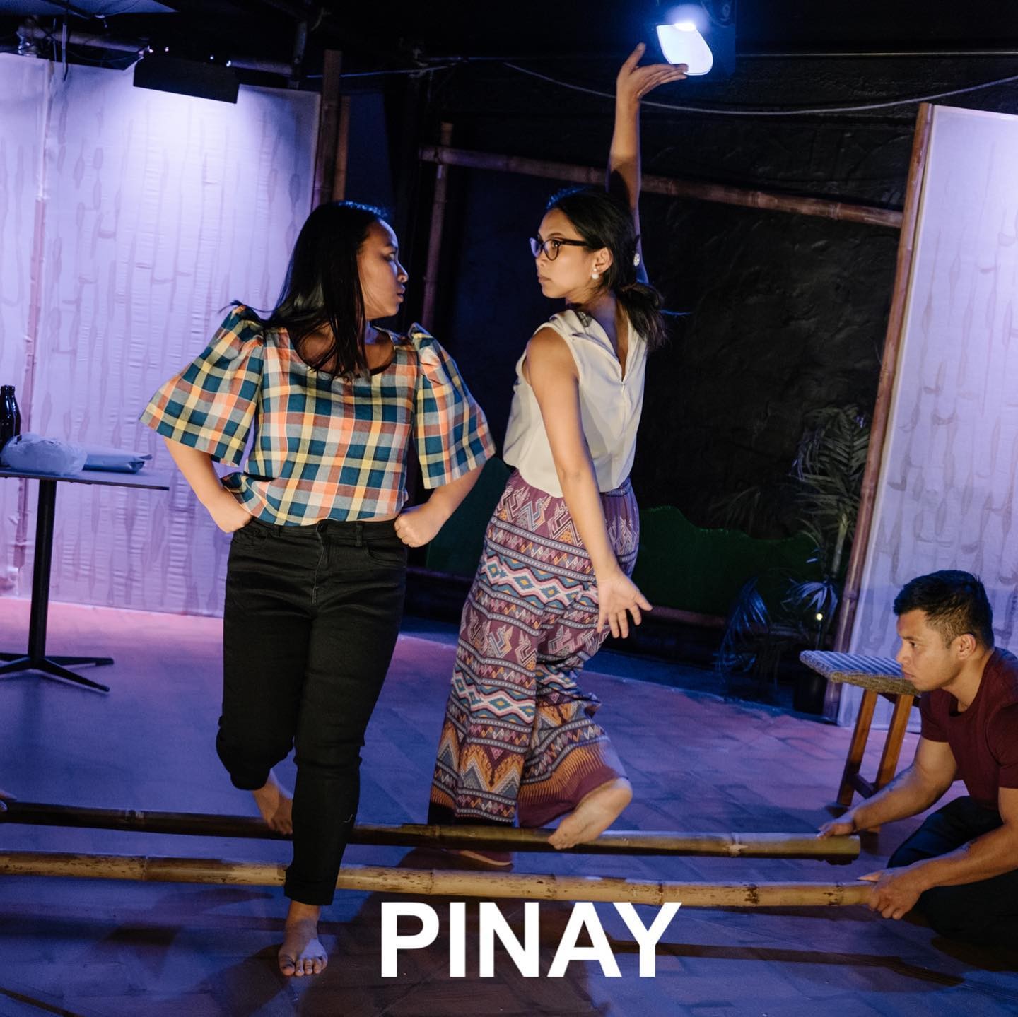 Three people performing a traditional Filipino folk dance involving two bamboo sticks. Two people are dancing, while one person is holding the sticks