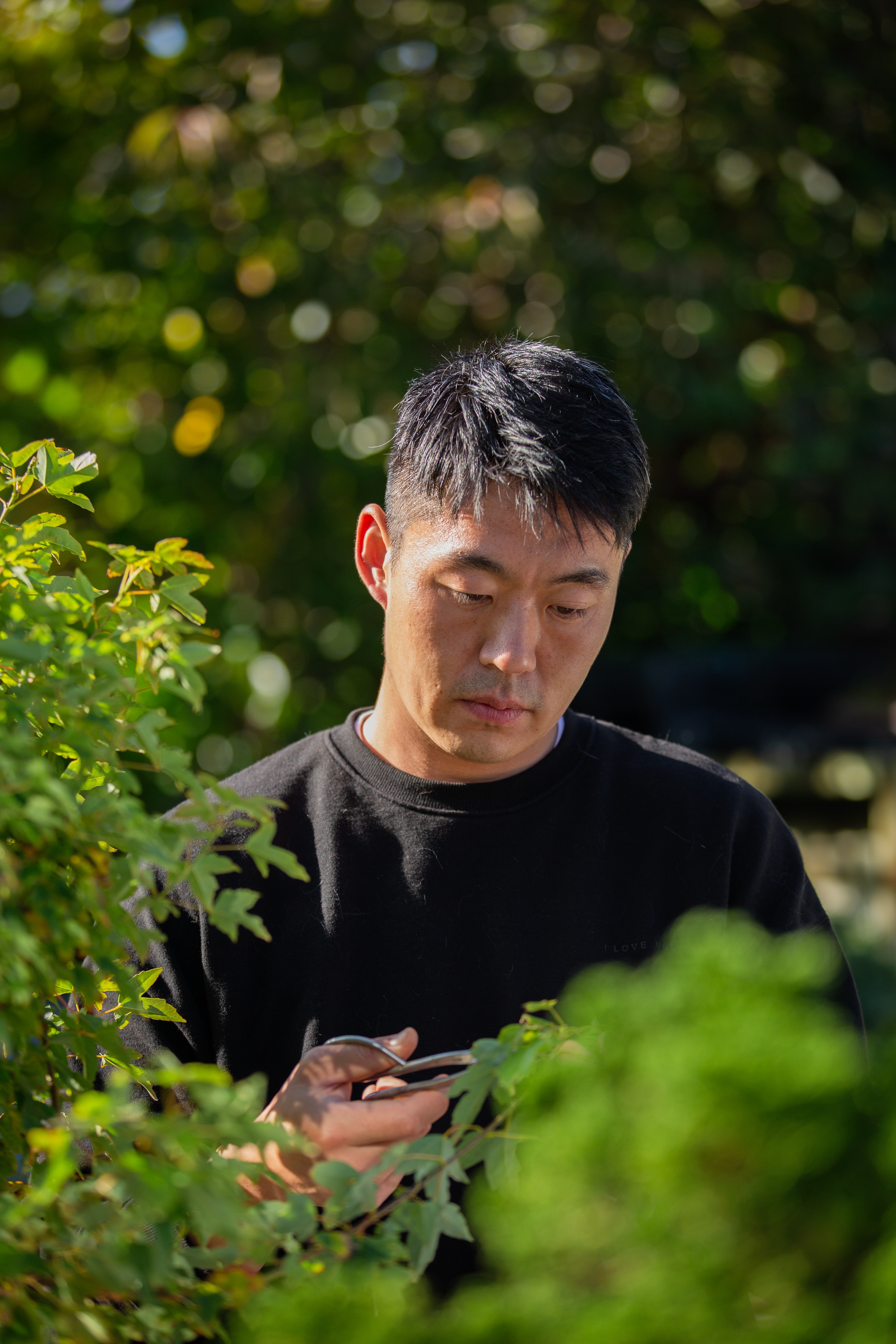 A man with short black hair tends to bonsai outdoors