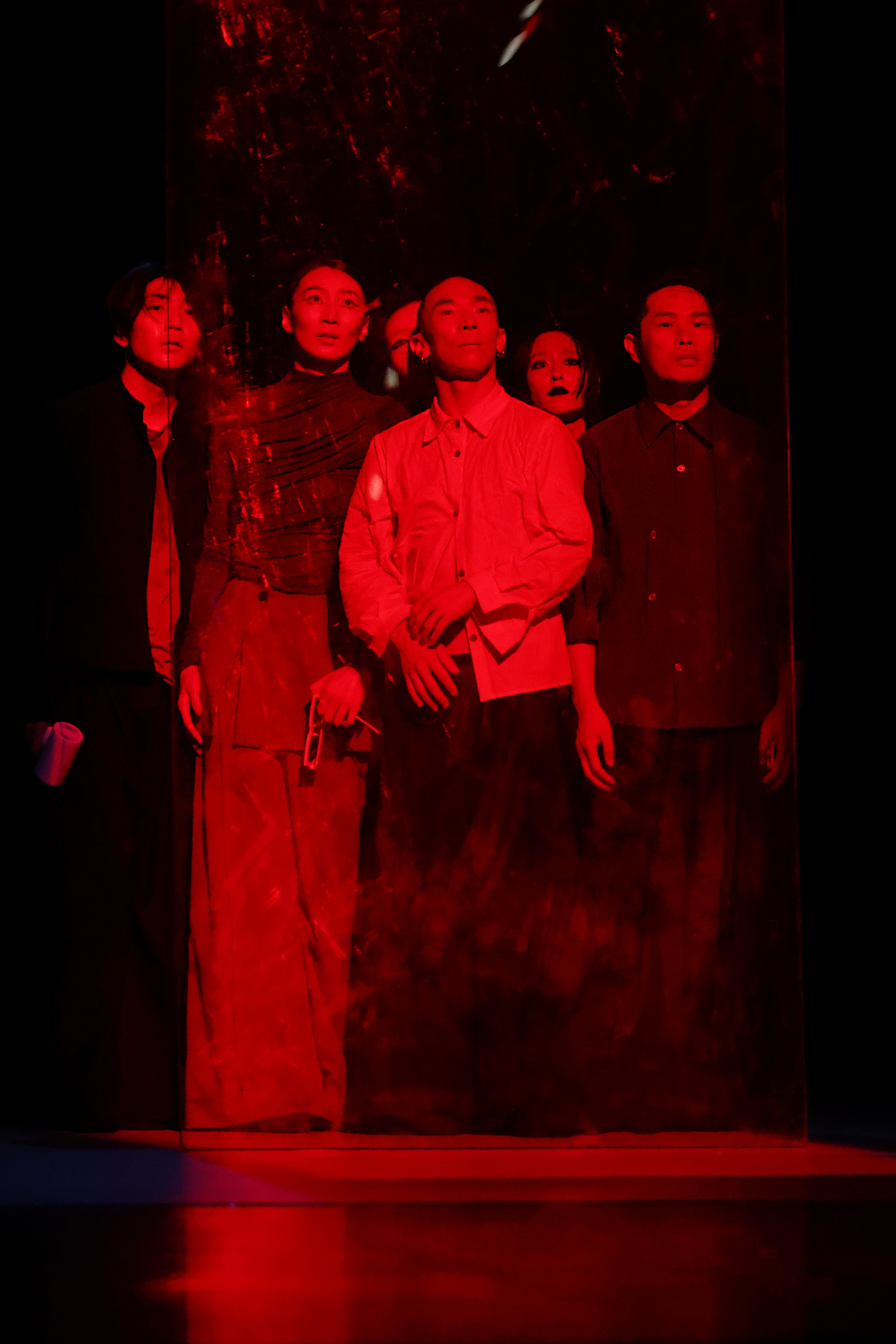 A group of performers stand huddled together under red lighting.