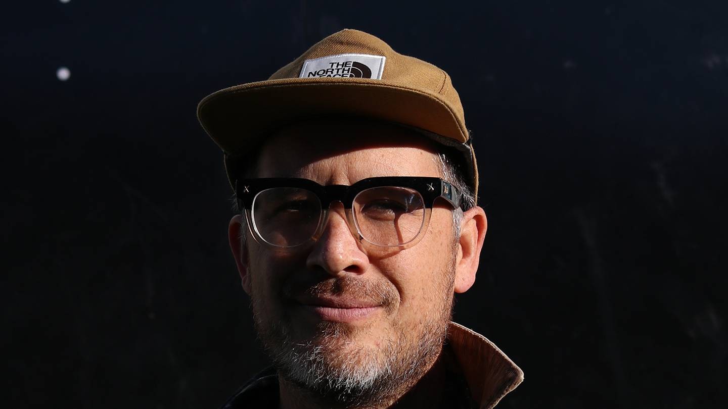 A man with glasses, a cap, and a greying beard smiles at the camera.