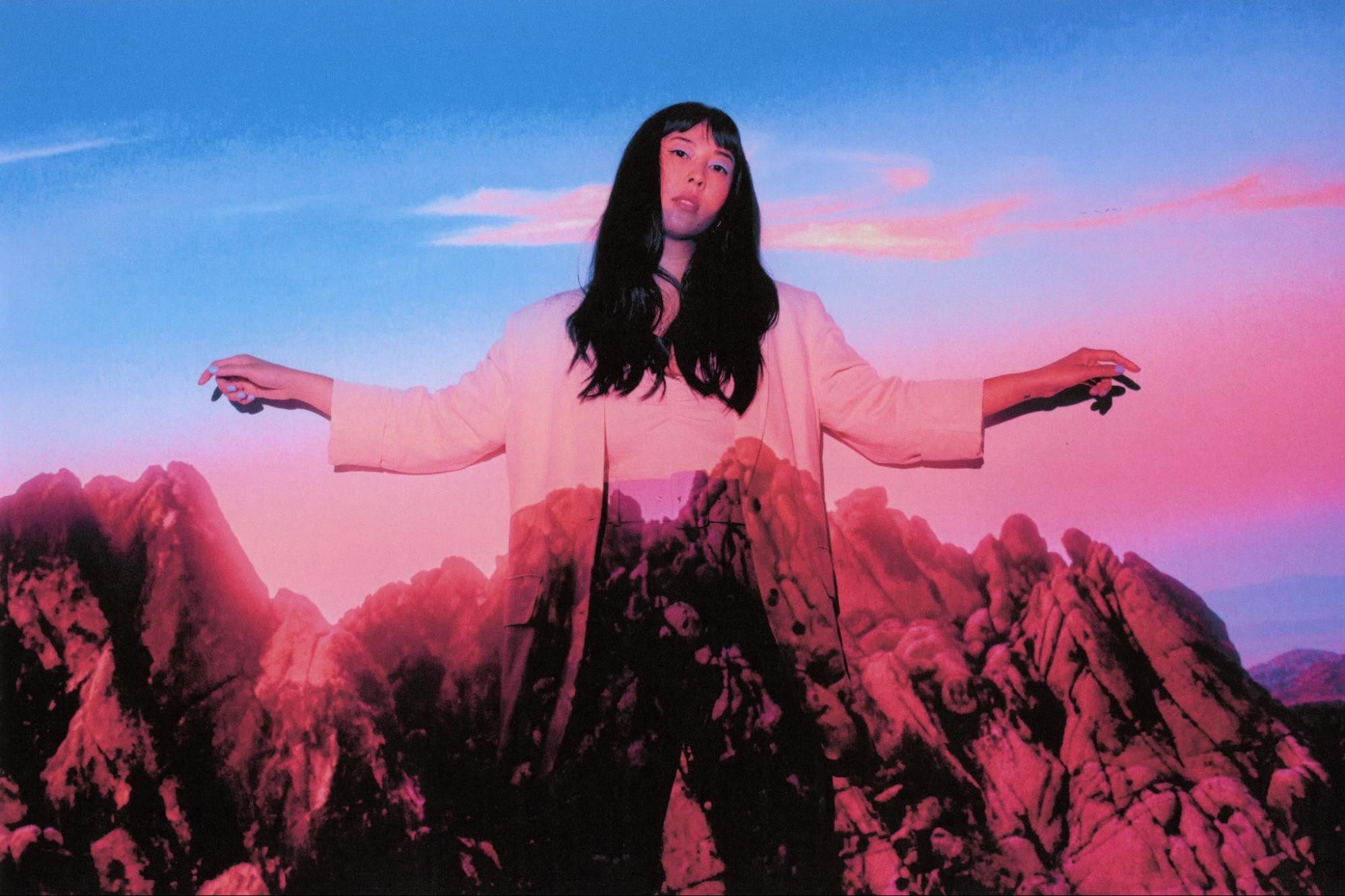A woman wearing white with a pink and blue mountainous sunset projected onto her