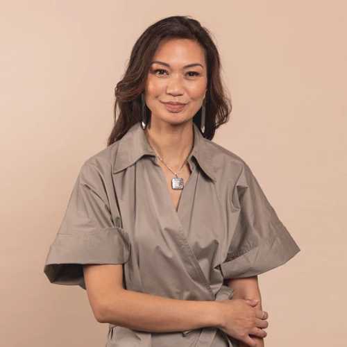 A woman with brown hair and drop earrings in a khaki boiler suit 