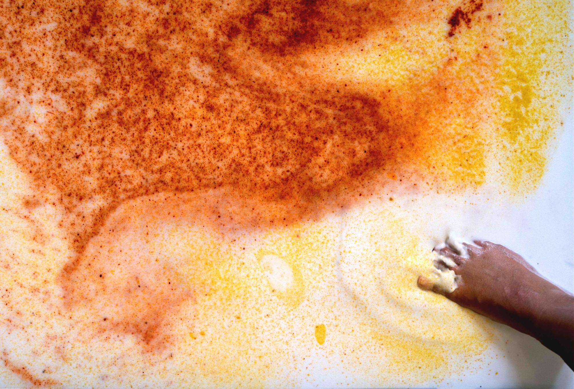 A brown foot dips its toes into a puddle of yoghurt sprinkled with yellow and orange spices.