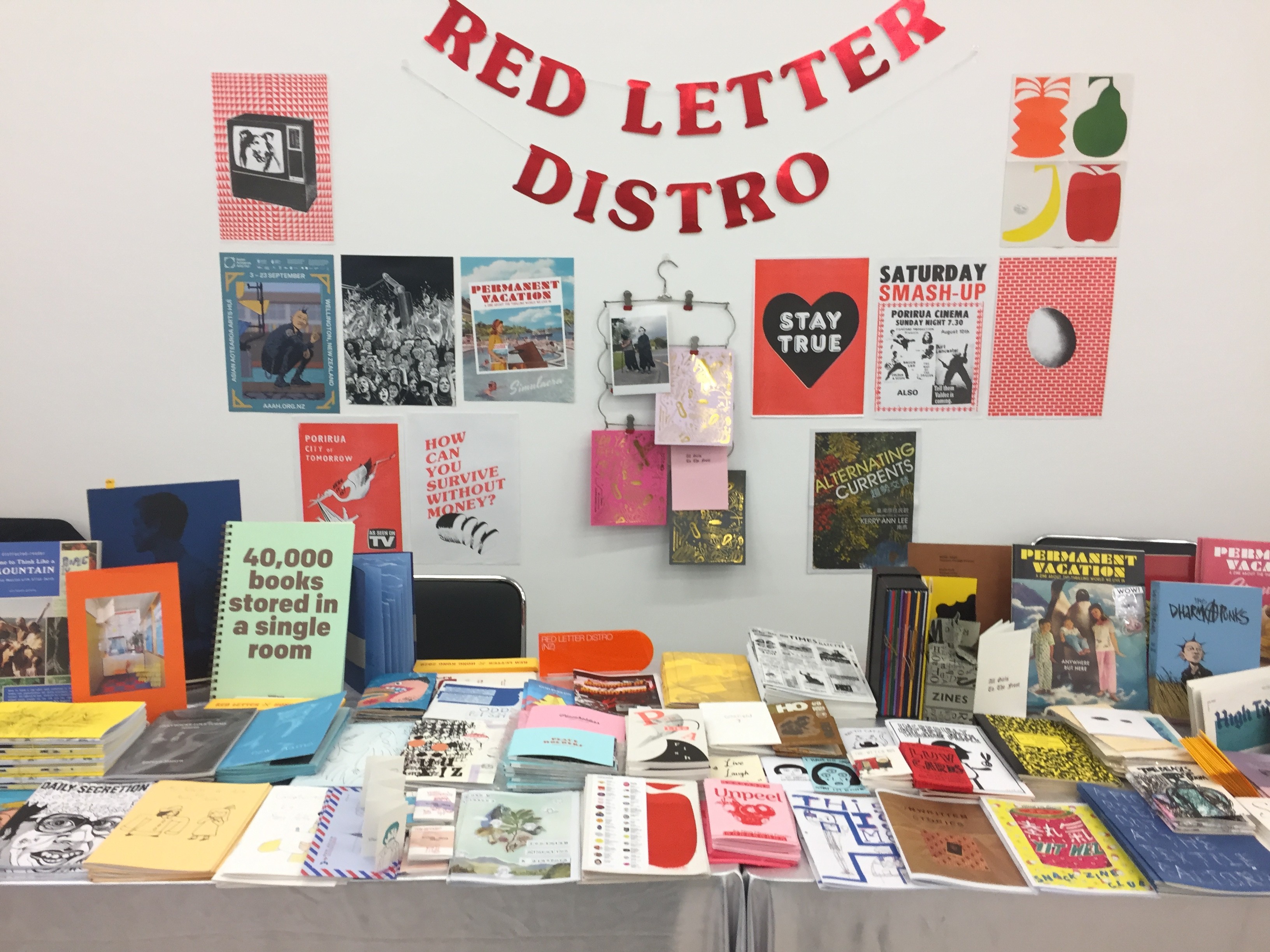A zine table with multiple colourful zines on display and a banner above with the words "Red Letter Distro" on red glossy paper. 