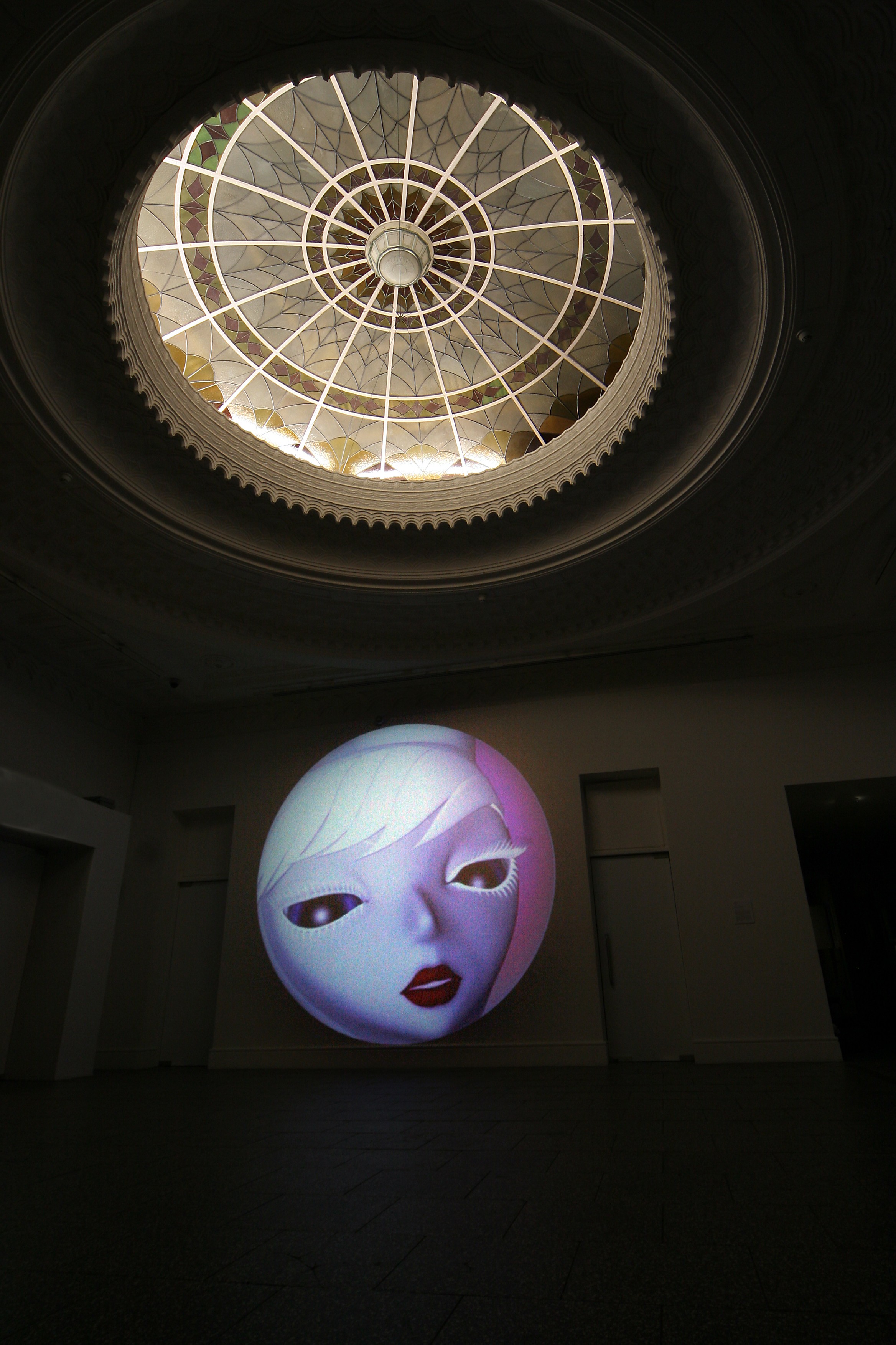 A round projection with a close up of an animated feminine face beneath a round ceiling dome.