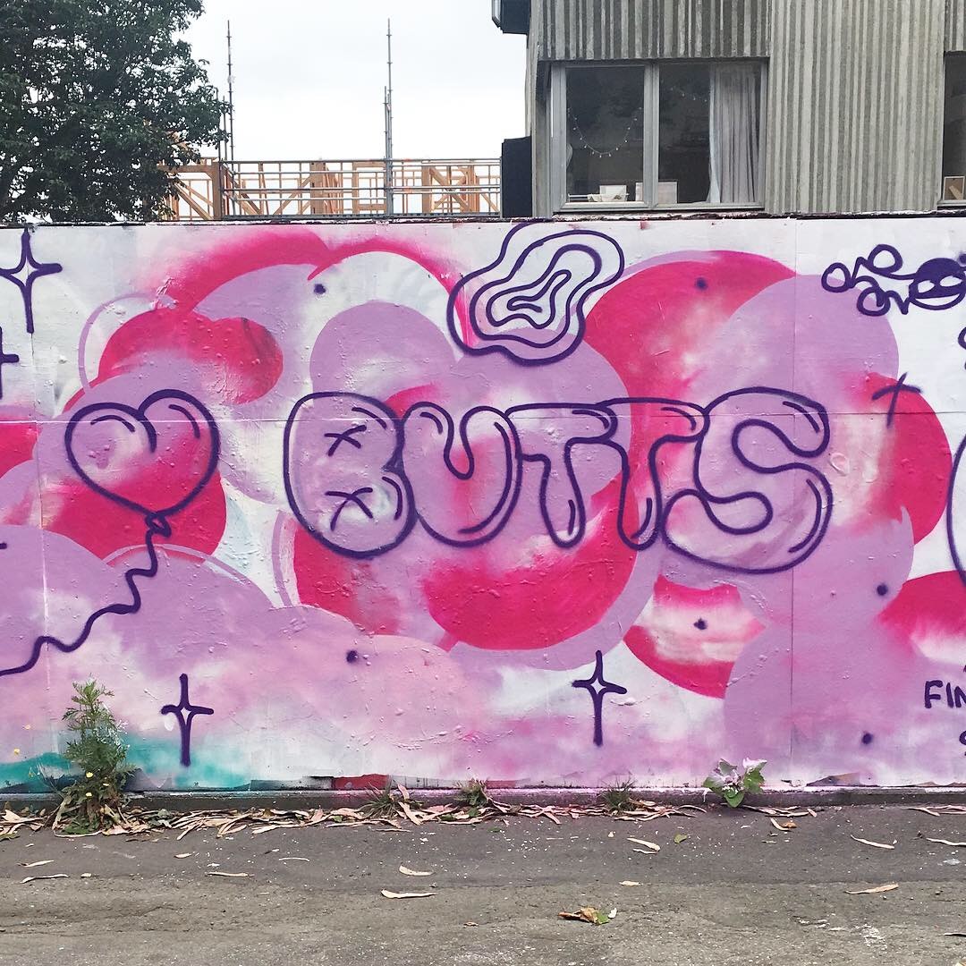 A pink and purple mural with the word "BUTTS" in the centre