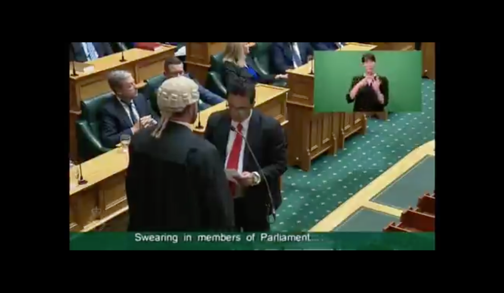 Sharma stands before a wigged official in Parliament.