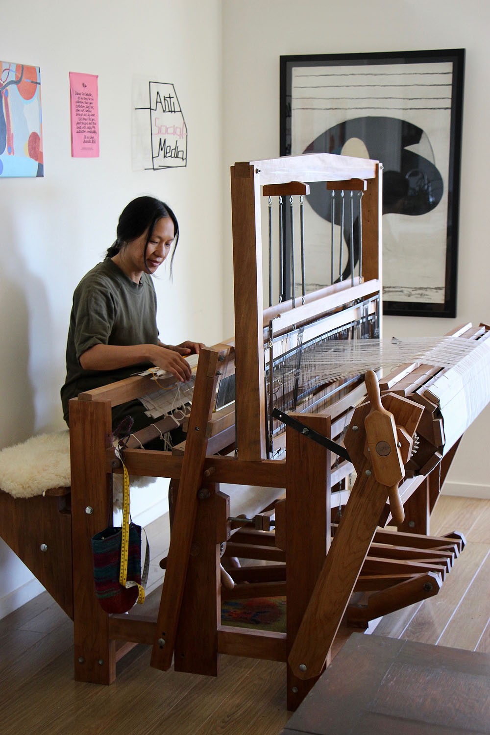 A woman with black hair sits at a large loom, working on a weaving.