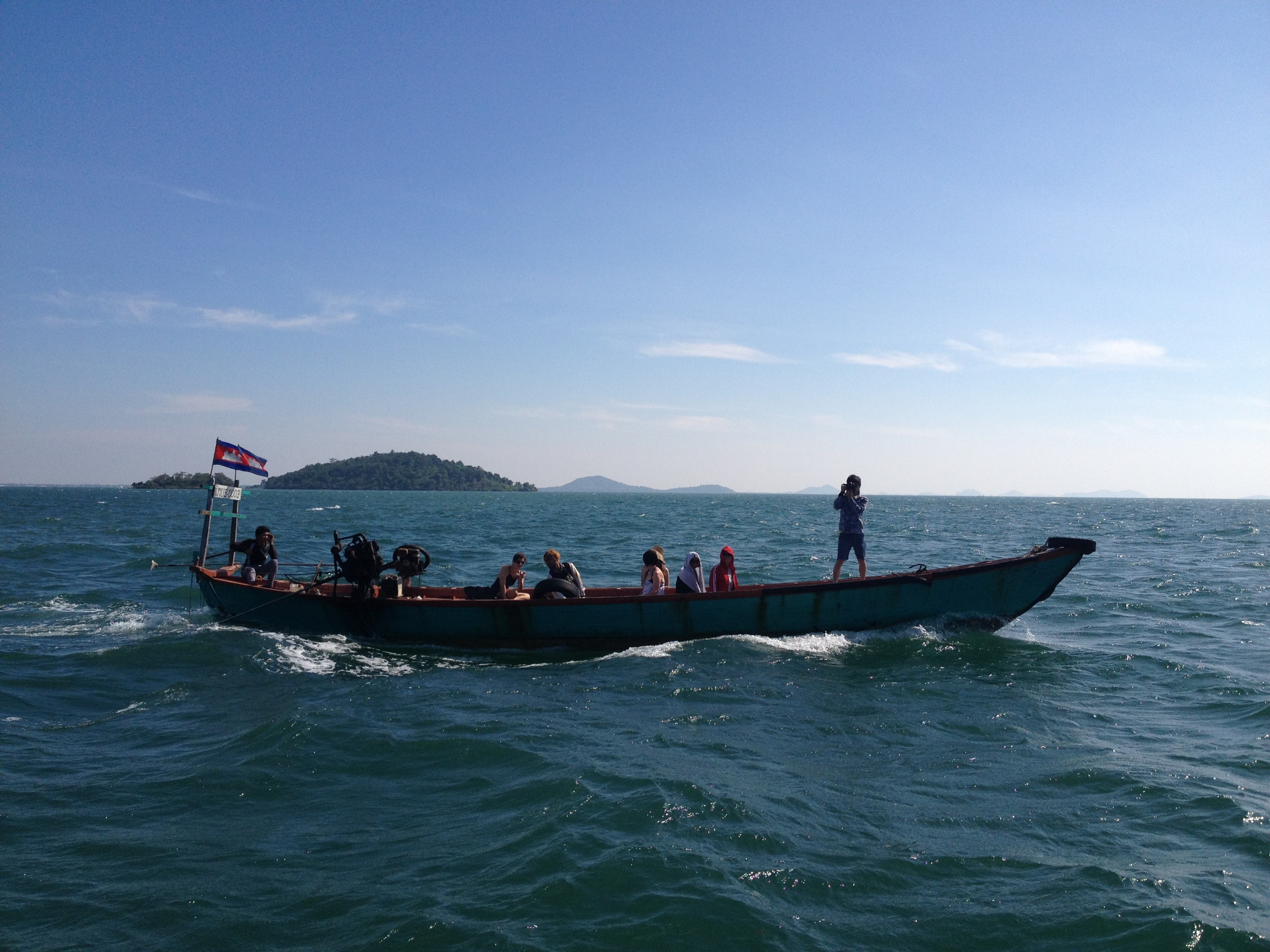 People in a long boat on the water in front of an island.