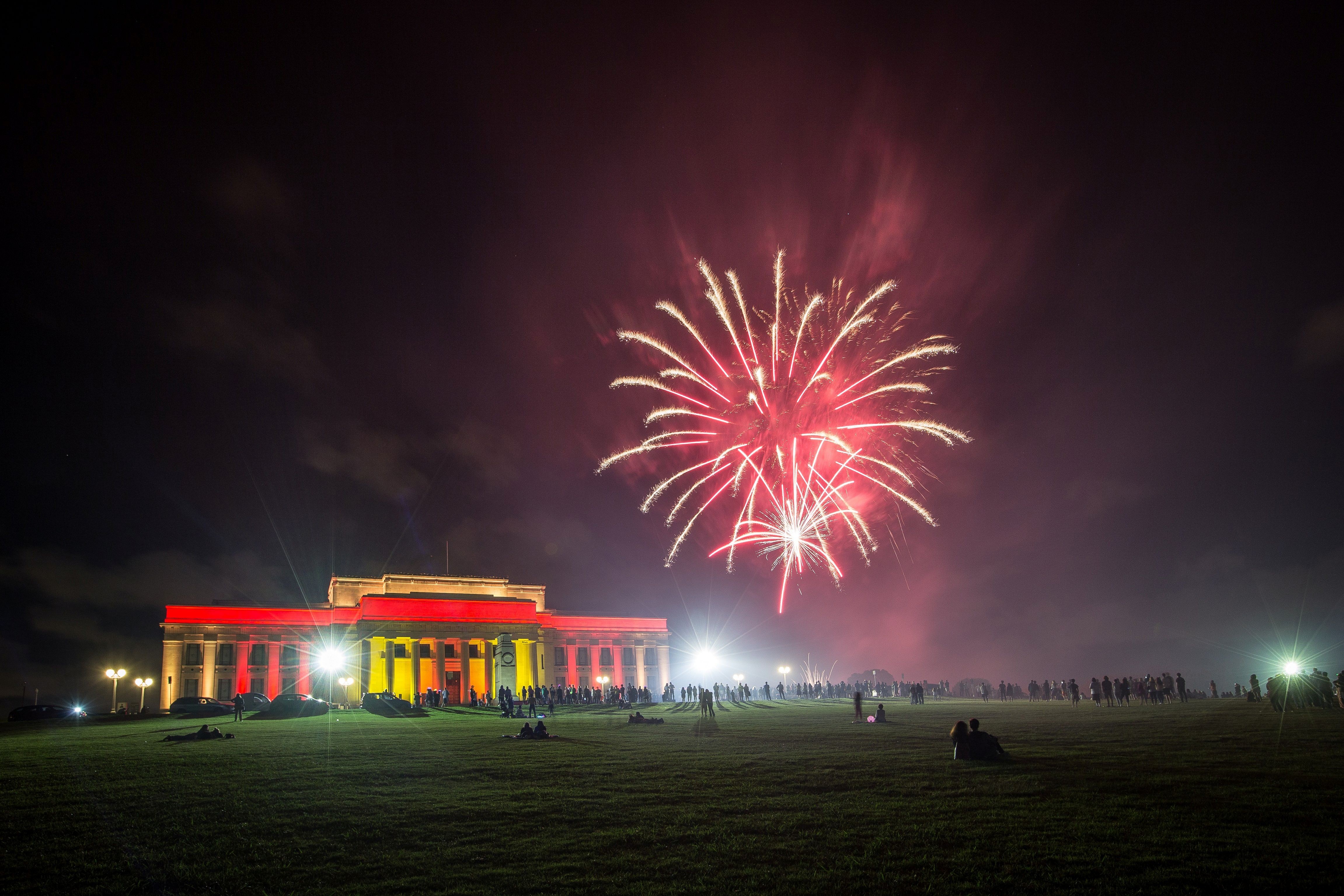 A building with coloured lighting with fireworks above