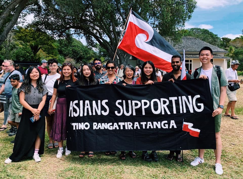 A group of people of Asian descent posing with a banner and a Tino Rangatiratanga flag