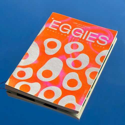 A bright orange zine with abstract egg patterns, photographed on a blue background.
