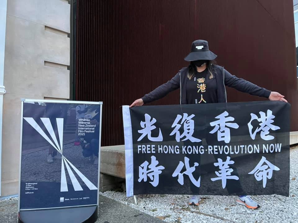 A masked protestor holds a Free hong Kong banner outside a cinema next to a Film Festival sign.