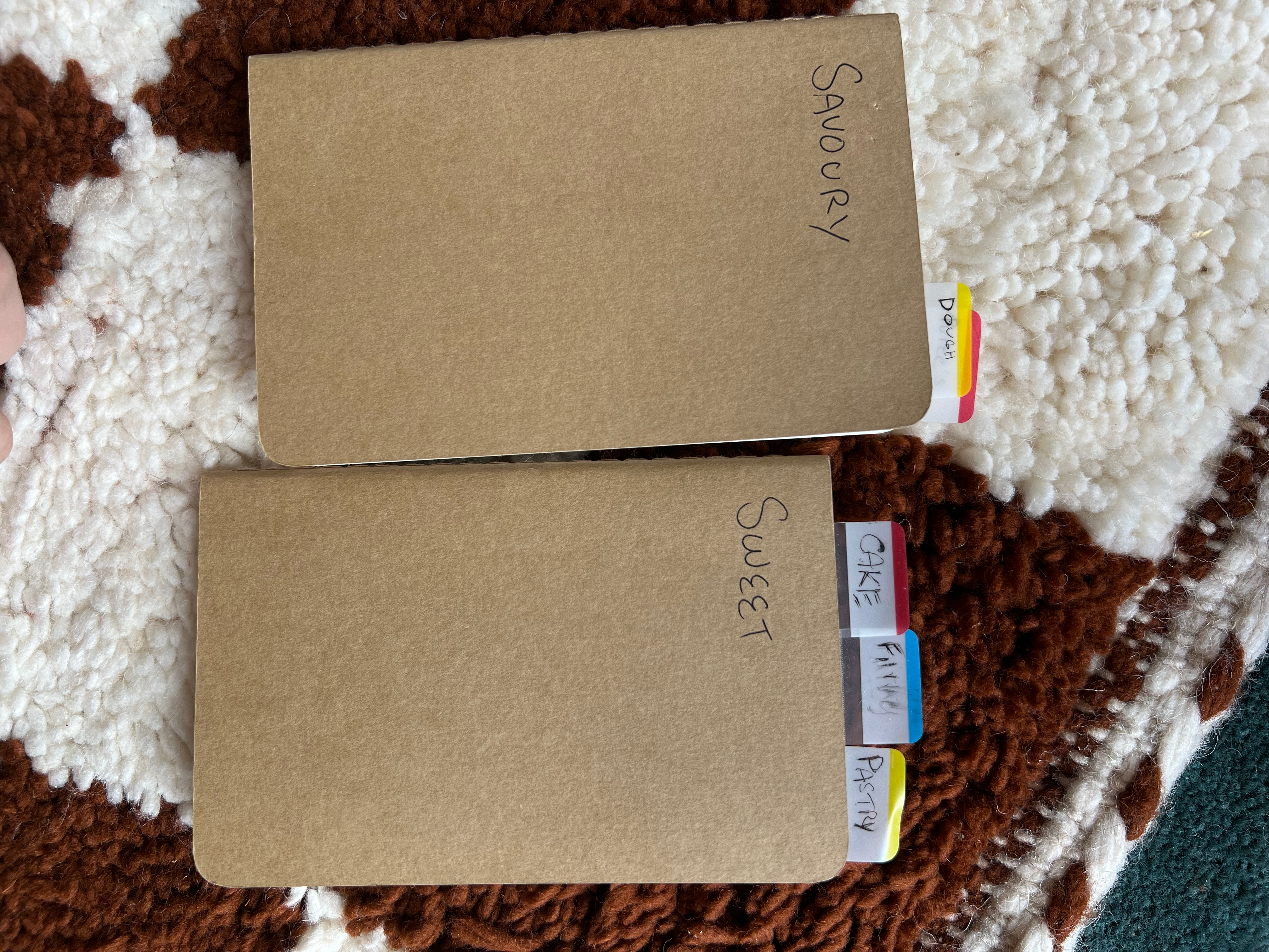 Two plain brown notebooks with tabs in them. One notebook has 'Savoury' and the other 'Sweet' in Sam's handwriting