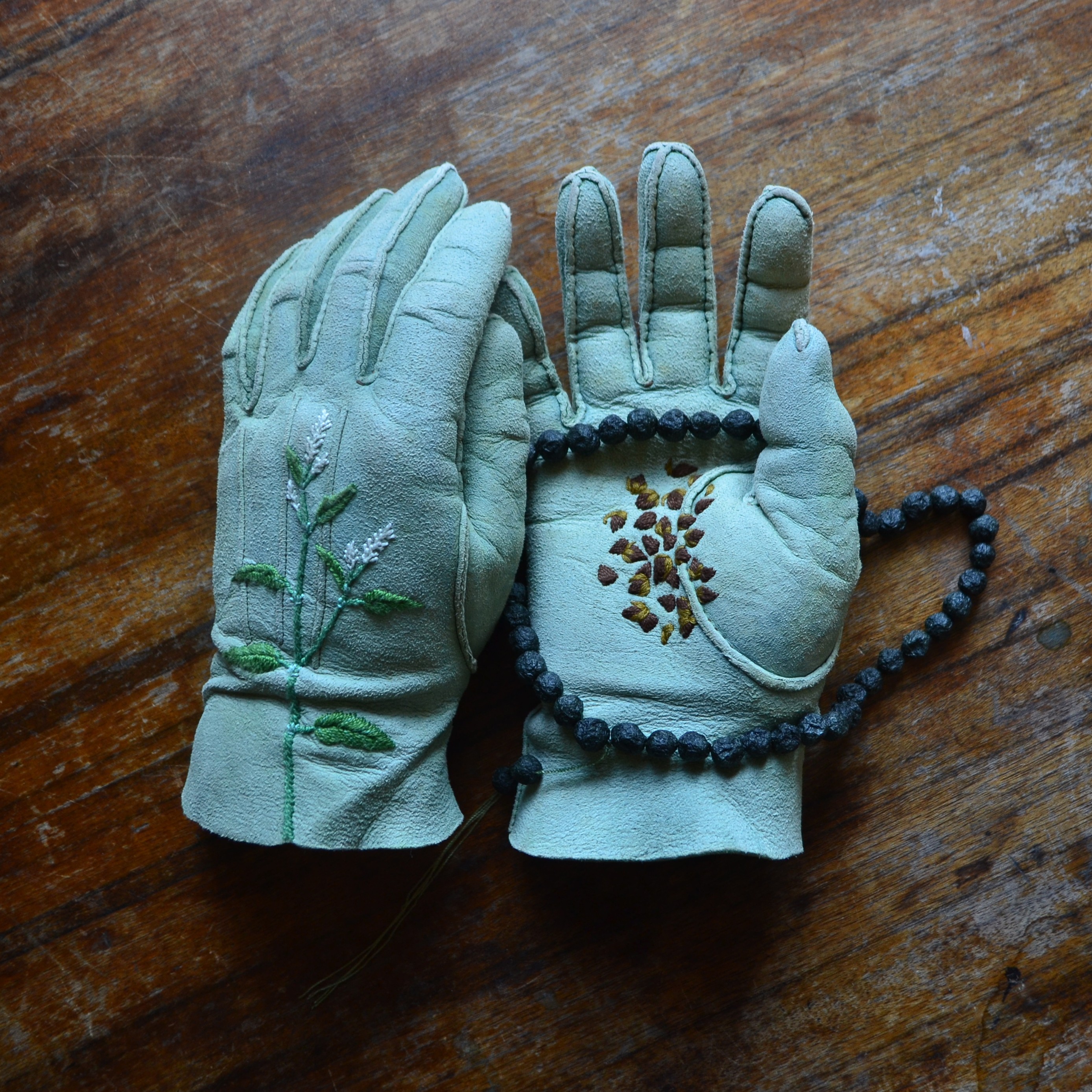 Pale blue leather gloves embroidered, holding a string of seeds.