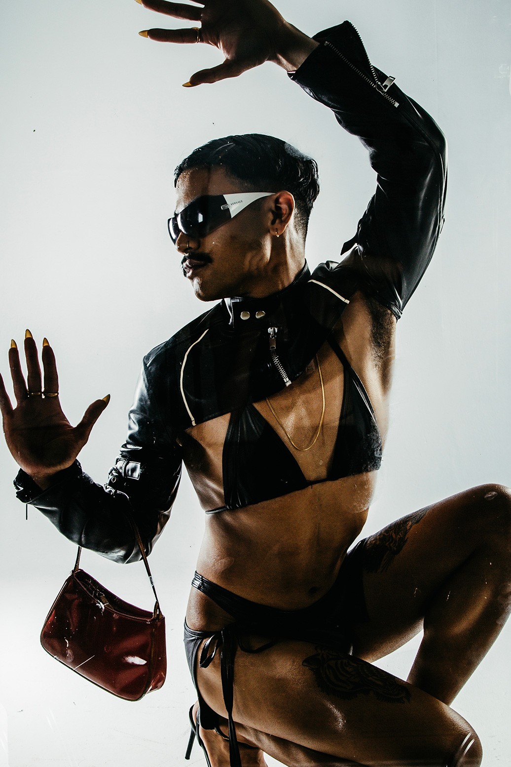 A gender bending model with a moustache and long nails wearing a skimpy leather skirt and bolero-style top with a bra-top