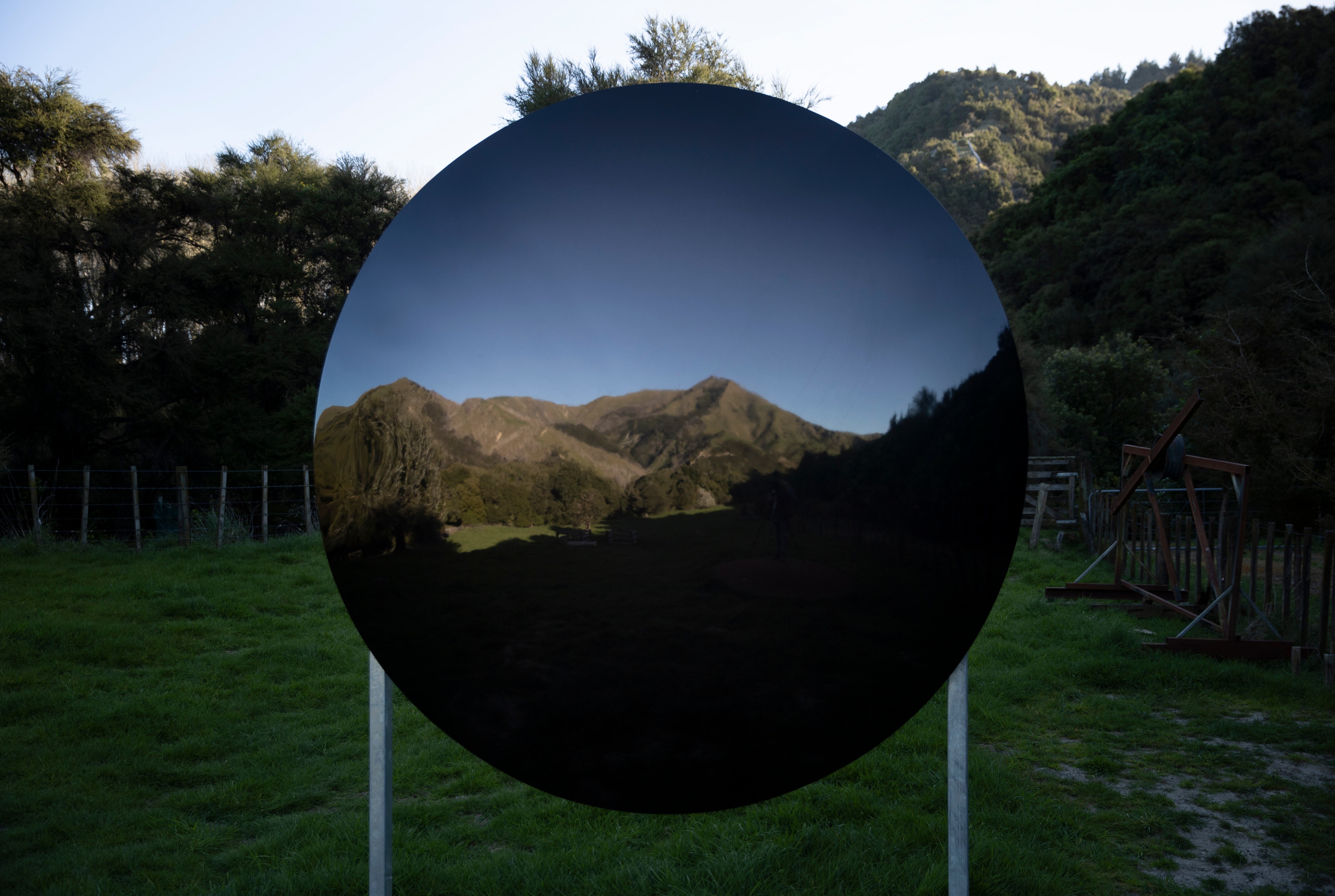 View of a hilly landscape reflected in a a curved piece of glass outdoors.