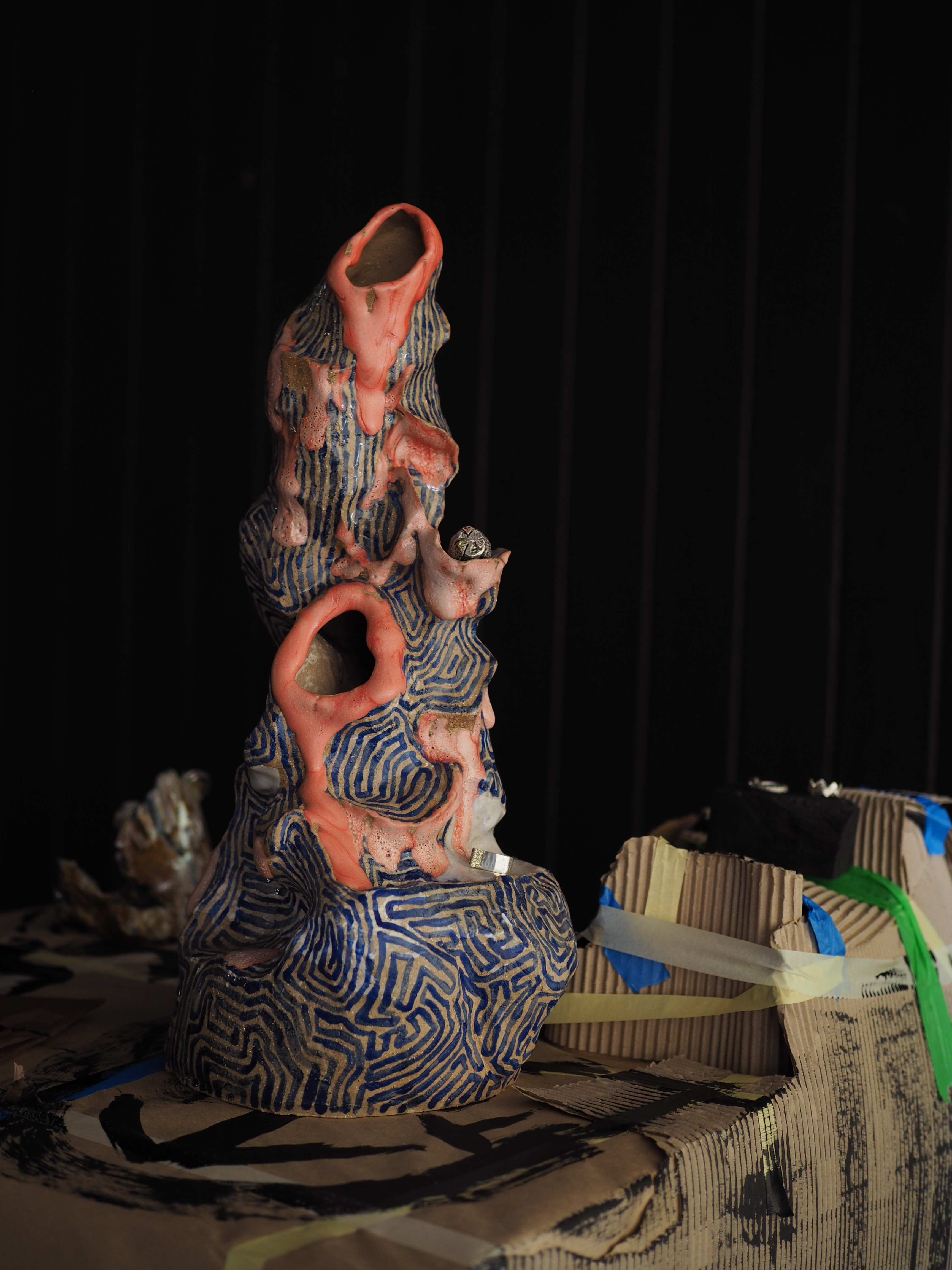 An organic sculpture with multiple holes outlined in orange and blue lines on the body