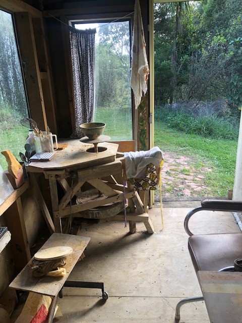 Interior corner of a desk with a clay pot being made, next to a door to a garden.