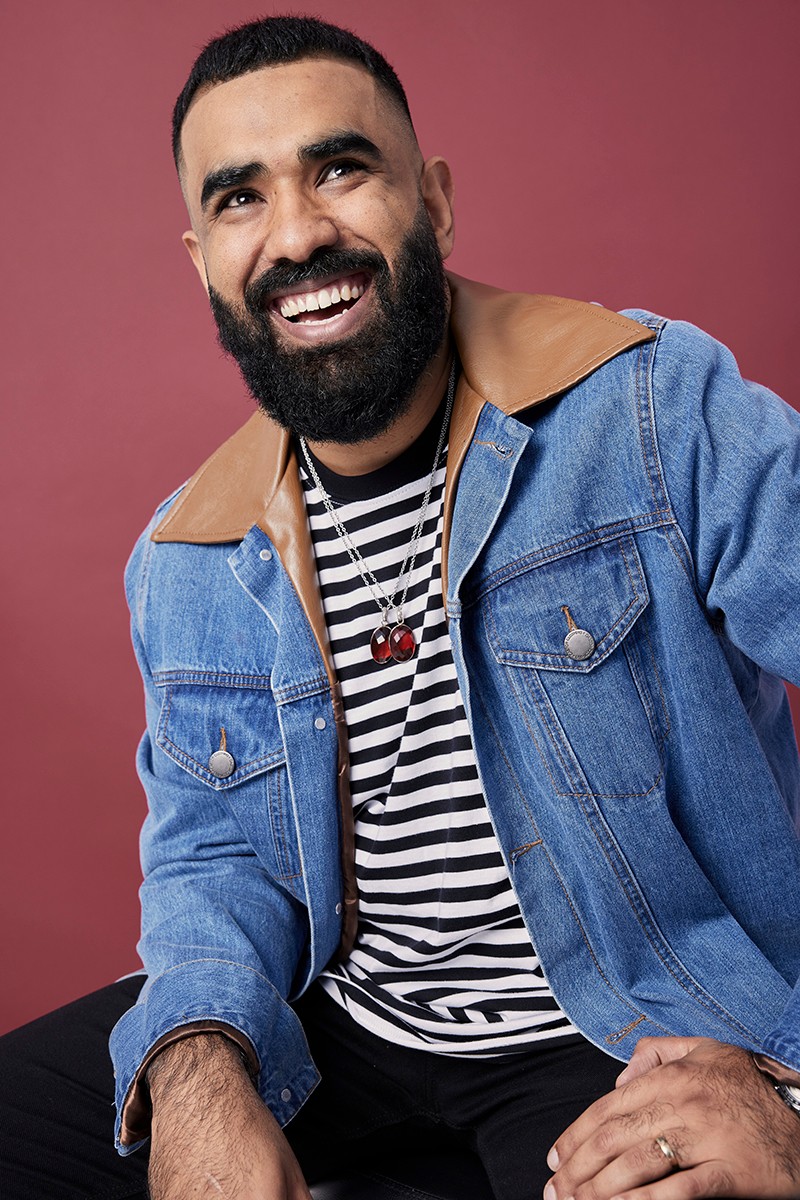 A man with a beard wearing a denim jacket and black-and-white striped shirt grinning at the camera