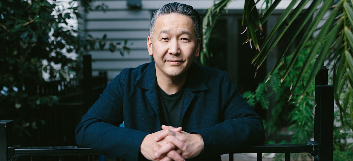 Kelvin Soh leans against a railing with hands folded, wearing a lapelled jacket.