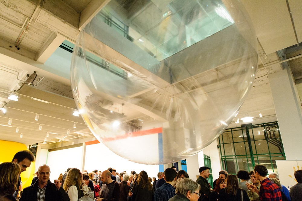 Lots of people socialising below a large translucent orb hanging from the ceiling in a large foyer space.