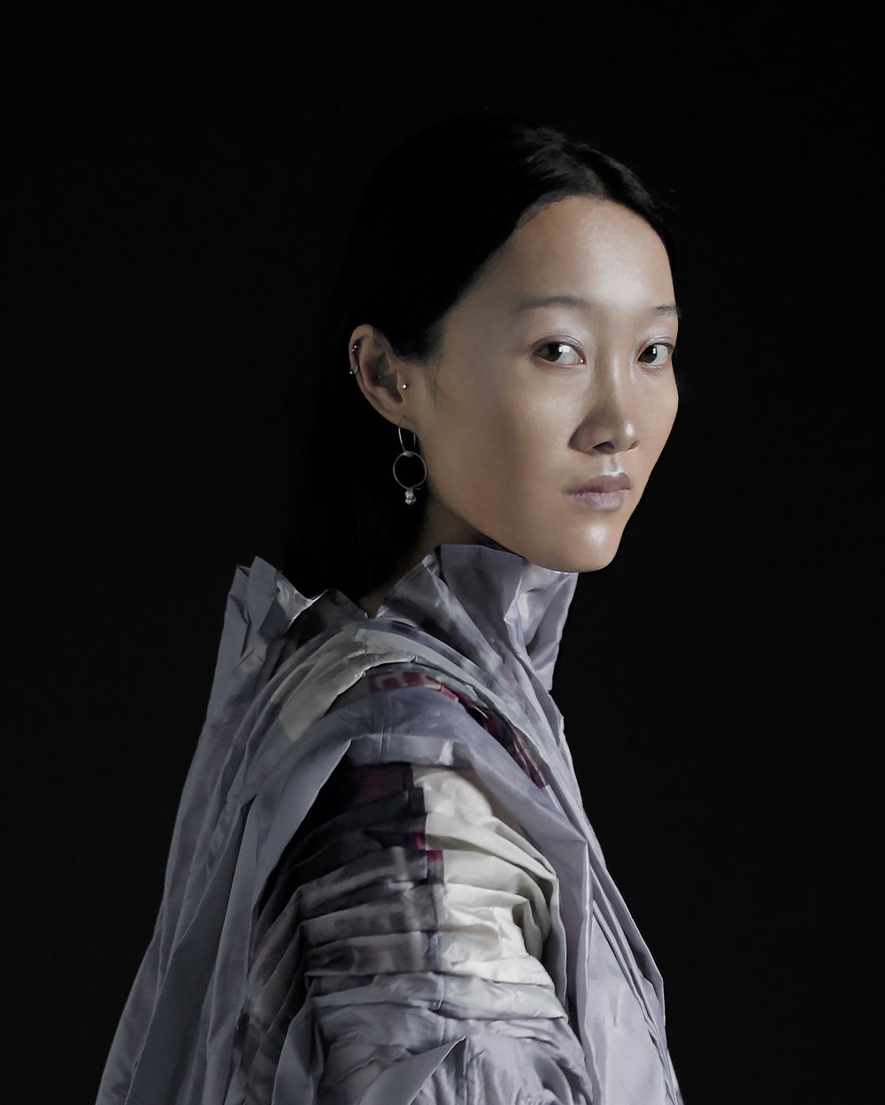 half body shot of an asian women wearing a draped and pleated lavender and mulberry top