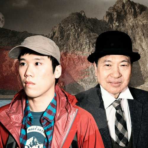 A young Chinese man in a red rain jacket and cap stands on a beach while a man in a suit stands behind him