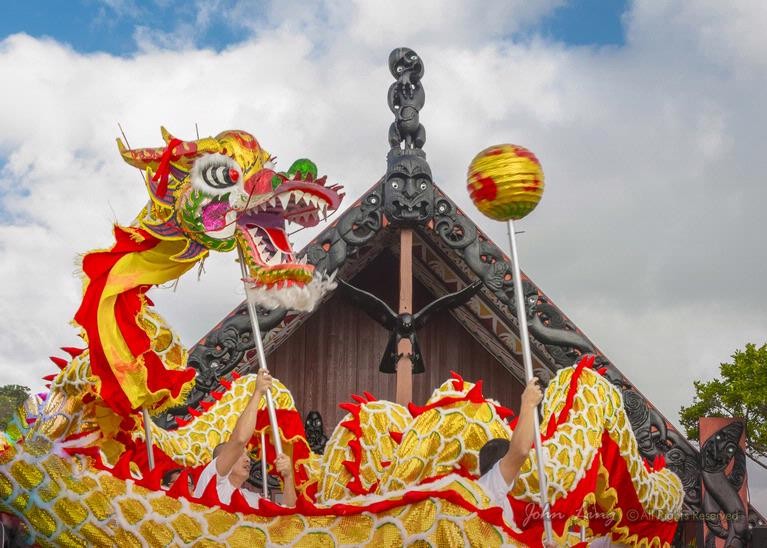 A Chinese dragon dance takes place in front of a carved wharenui.